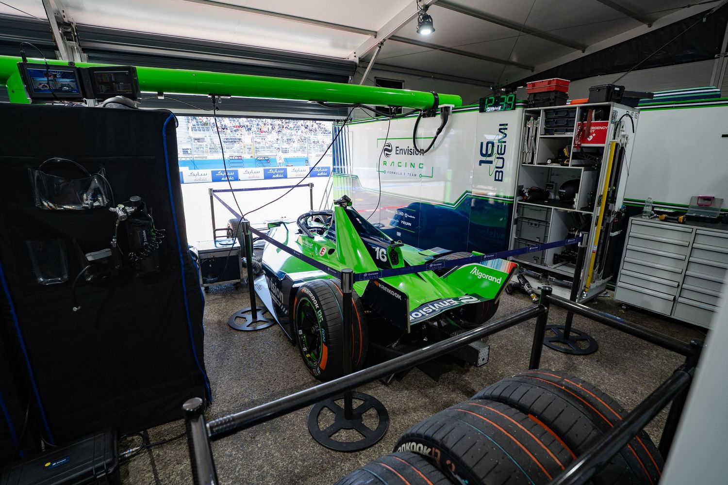 Green Formula E race car in a pit garage surrounded by tires and technical equipment during a racing event.