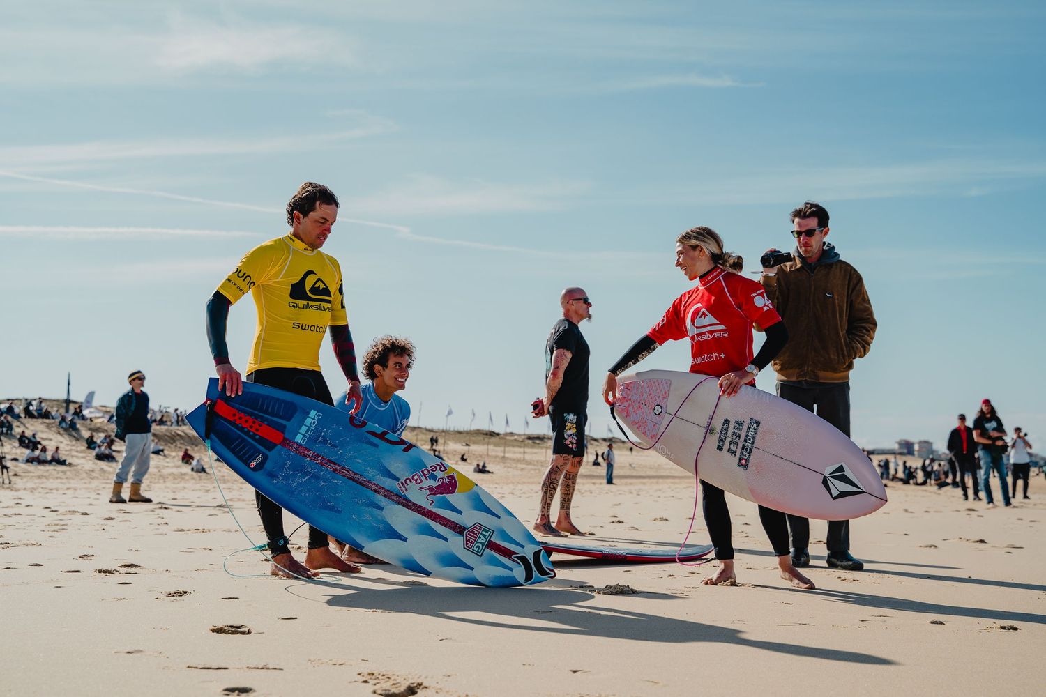 Group of surfers walking along a sandy beach carrying surfboards.