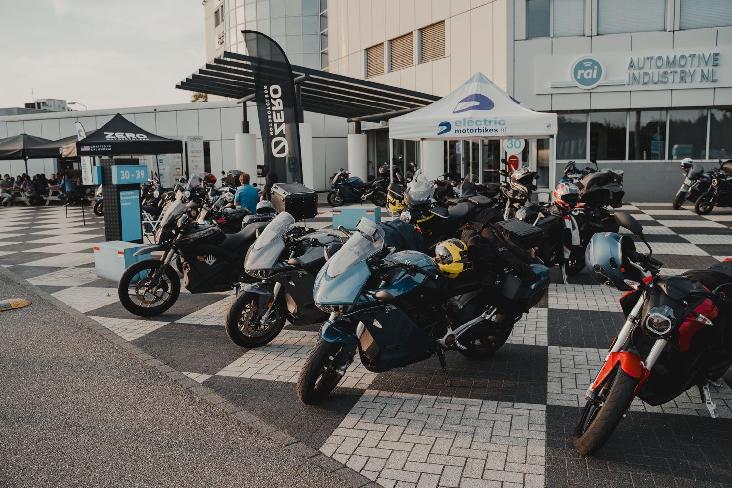 Row of parked motorcycles outside a modern building during a daytime event.