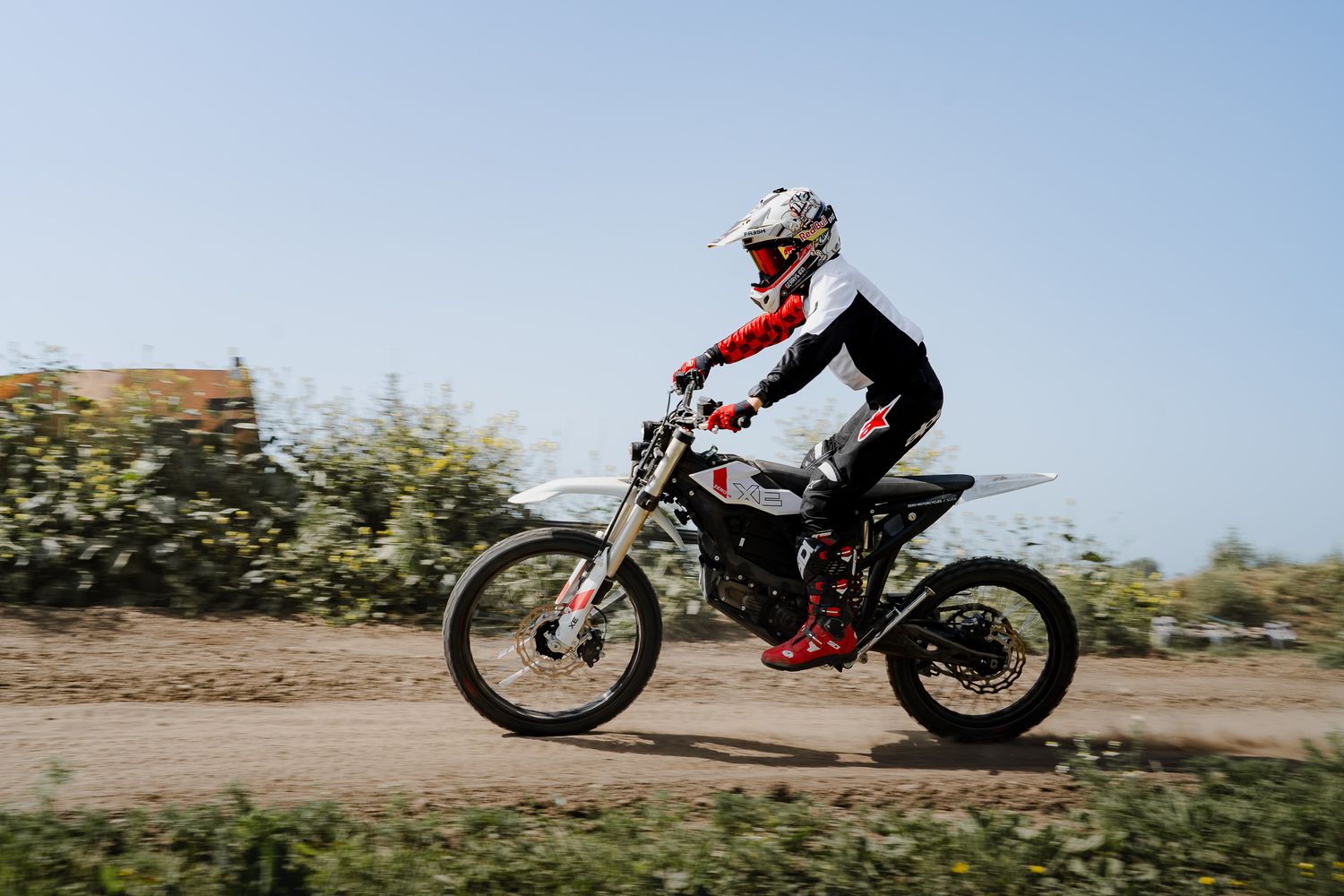 Motocross rider in white helmet and red gear racing on a dirt track on a white and red dirt bike.