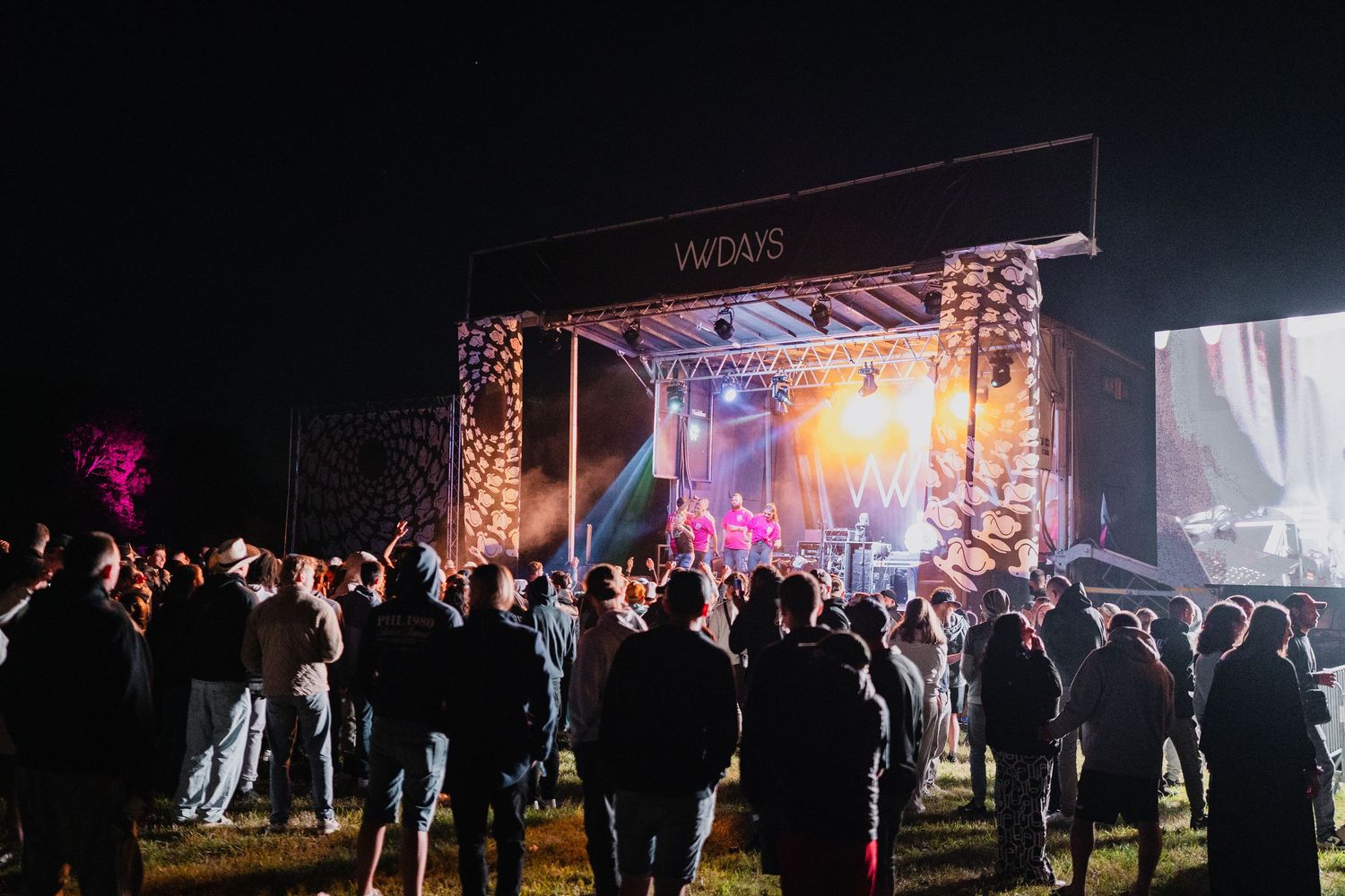 Crowd gathered at night for VVDAYS outdoor music festival with illuminated stage and performers.