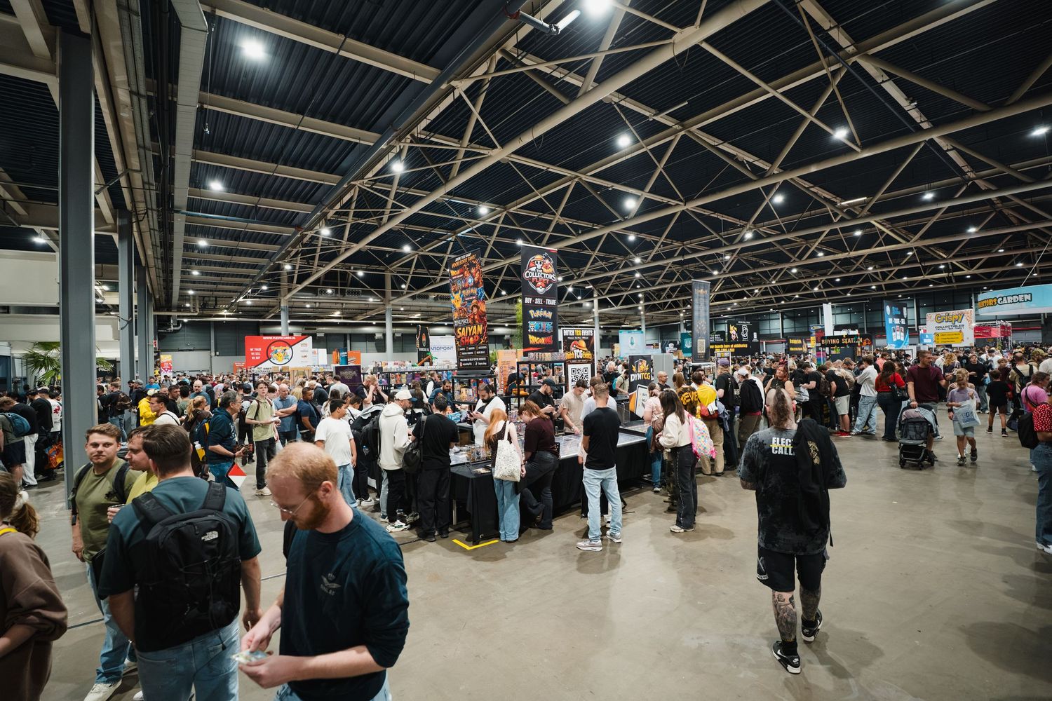 Large crowd of people browsing vendor booths inside a spacious convention hall with high ceilings and bright lights.