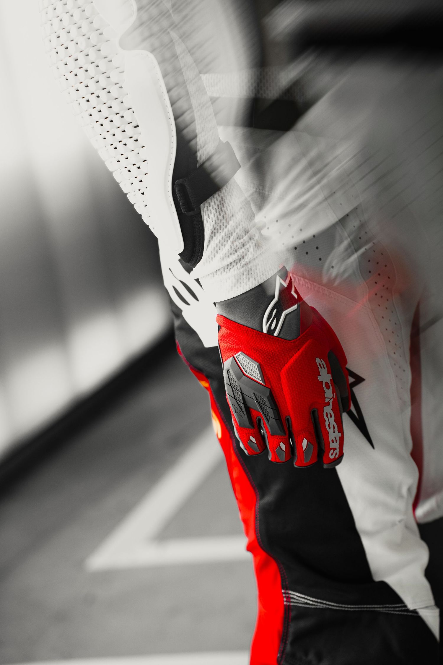 Alpinestars motorcycle racing suit in red, black, and white with motion blur effect.