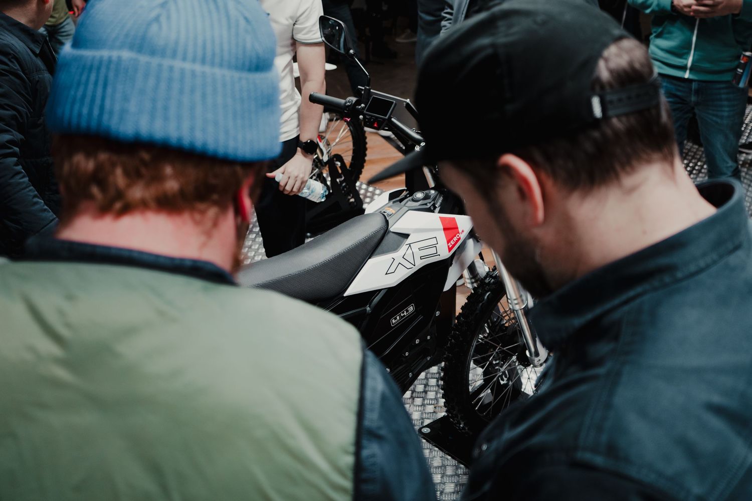Motorcycle enthusiasts gather at an indoor showroom examining bikes on display.