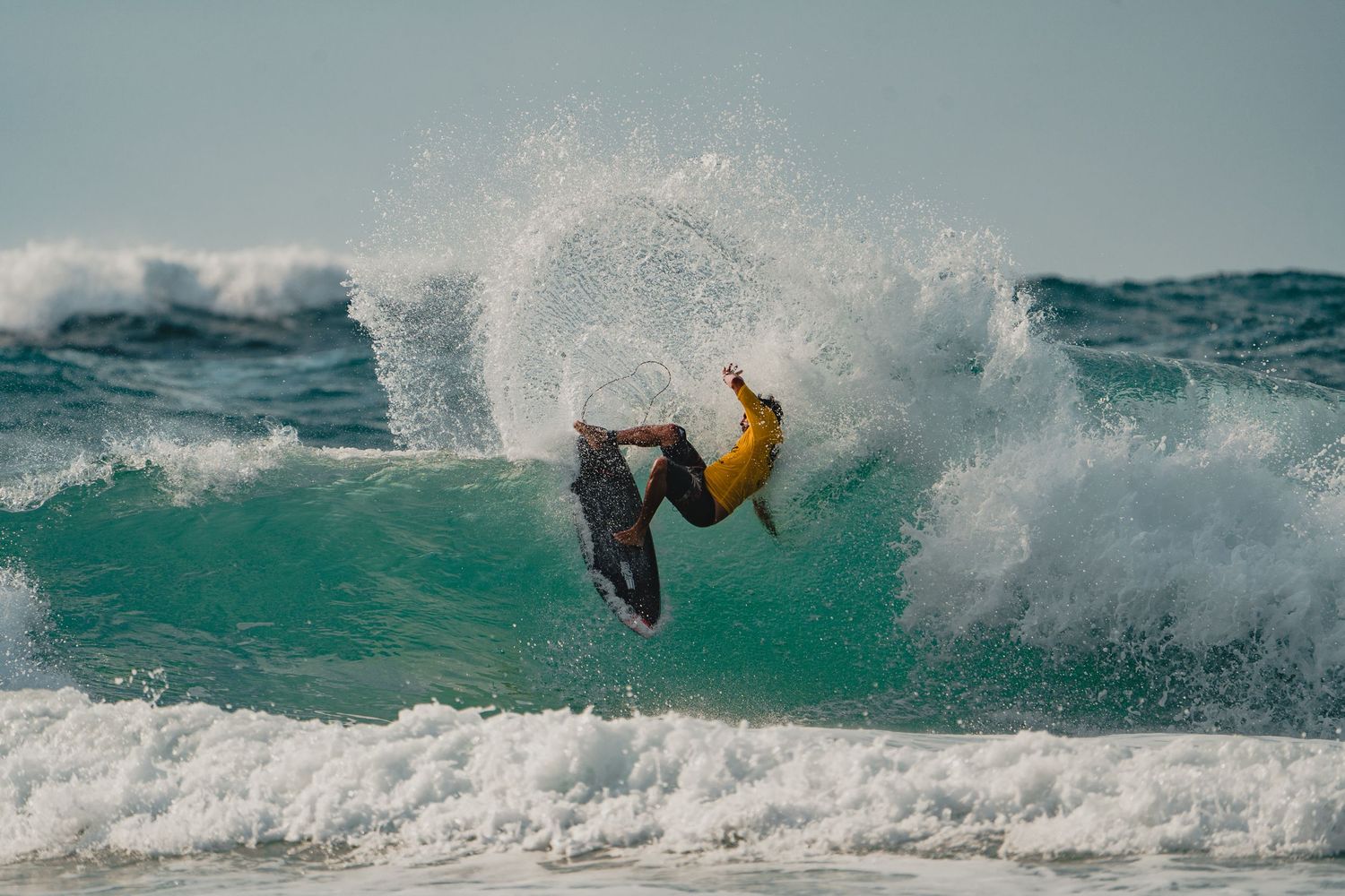 A surfer executes an inverted aerial maneuver over a breaking wave.
