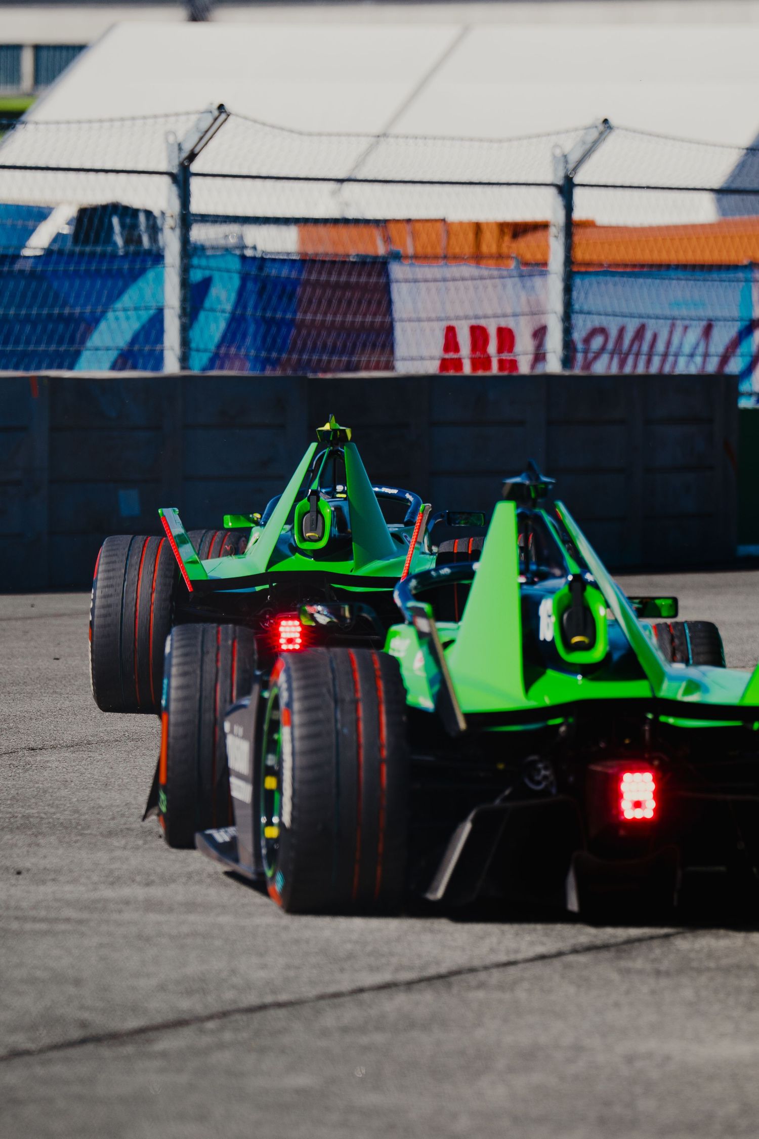 Two green Formula E electric racing cars compete on track at an ABB Formula E Championship street circuit event.