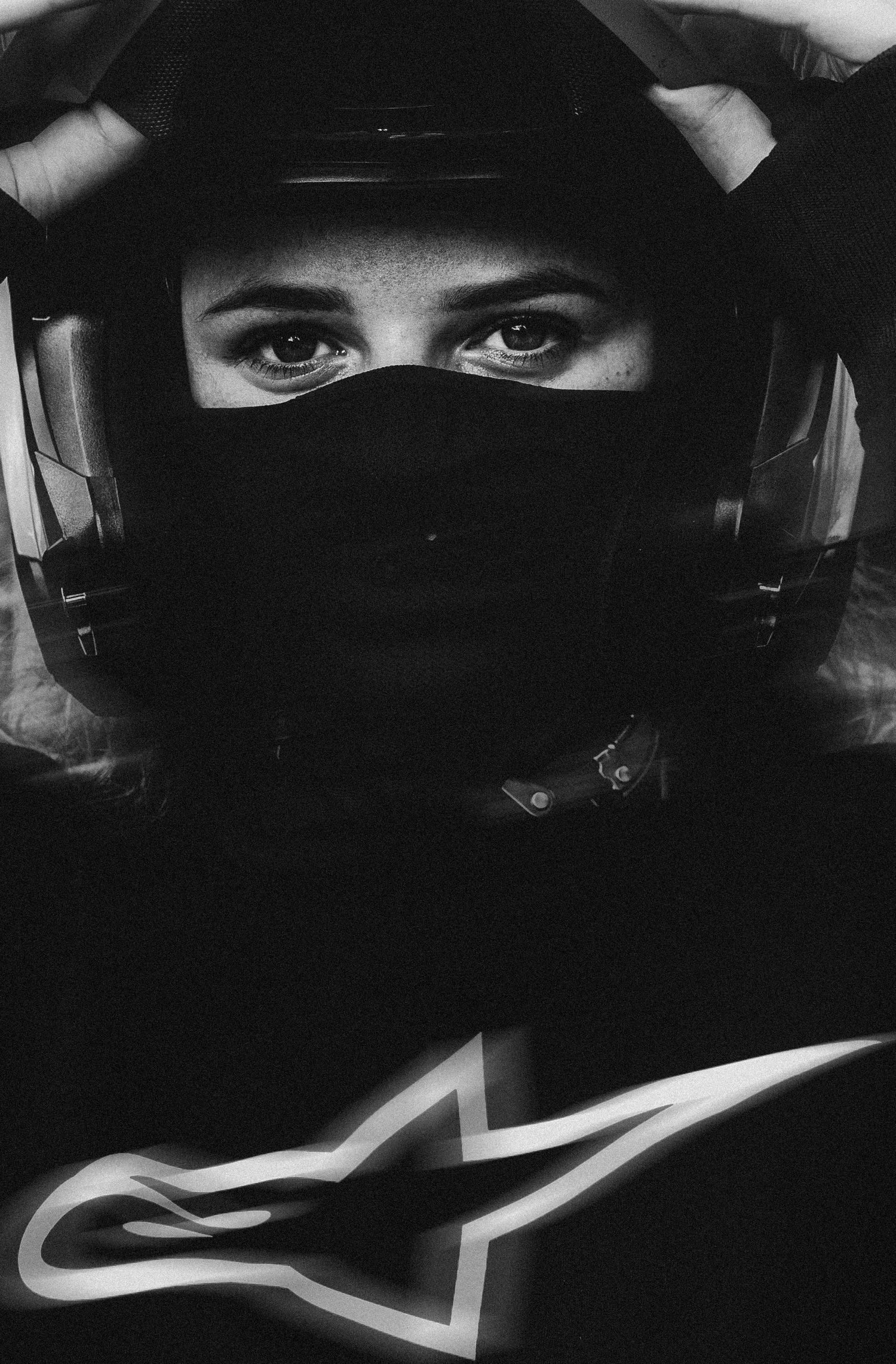 Black and white portrait of a person wearing an Alpinestars jacket and motorcycle helmet with visor up.