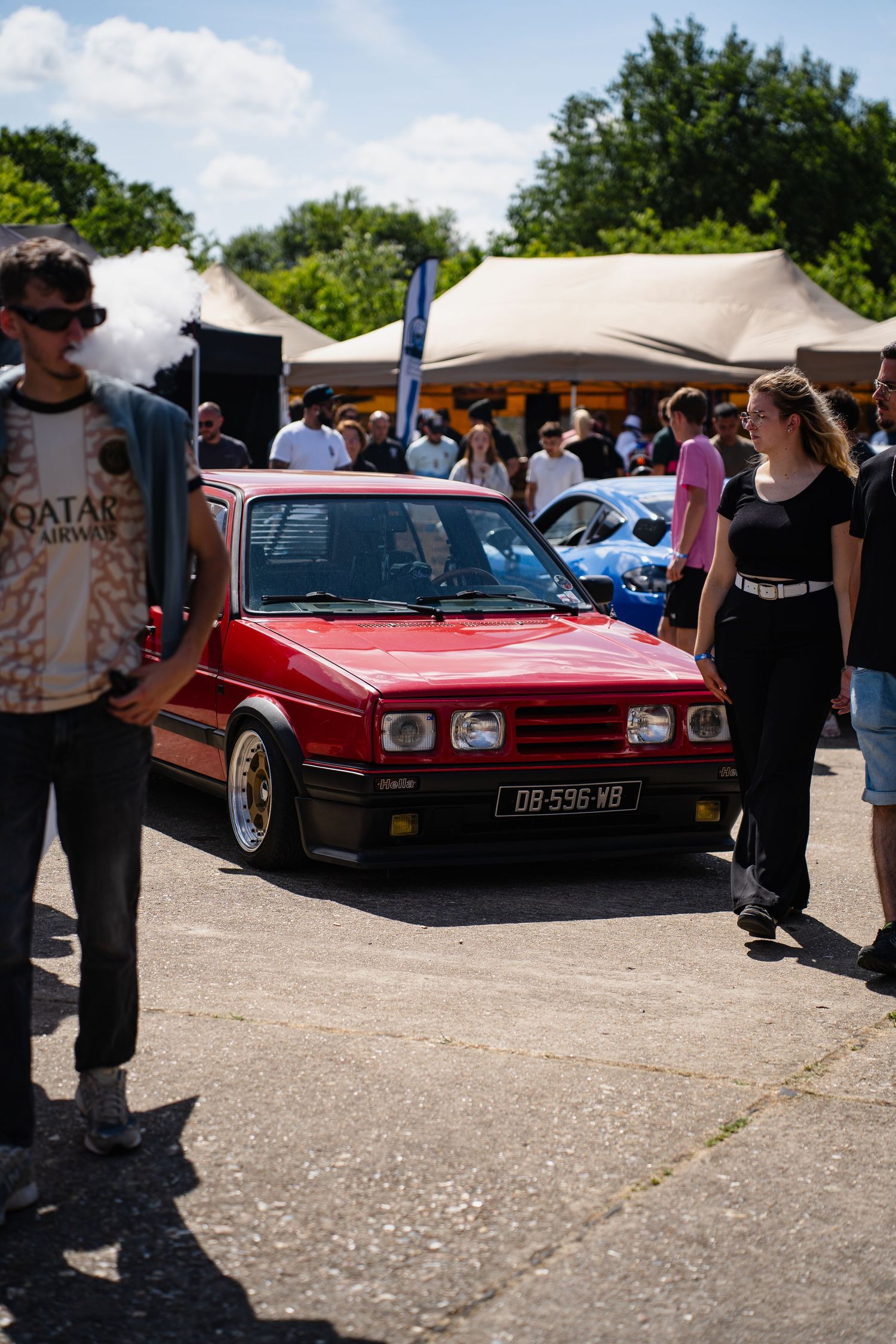 Red vintage Volkswagen Polo at an outdoor car show, surrounded by spectators on a sunny day.