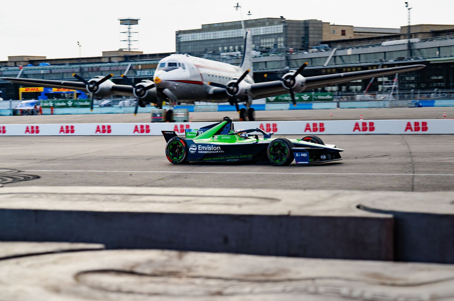 Formula E electric race car speeds past a vintage propeller aircraft at the ABB FIA Formula E street circuit race.