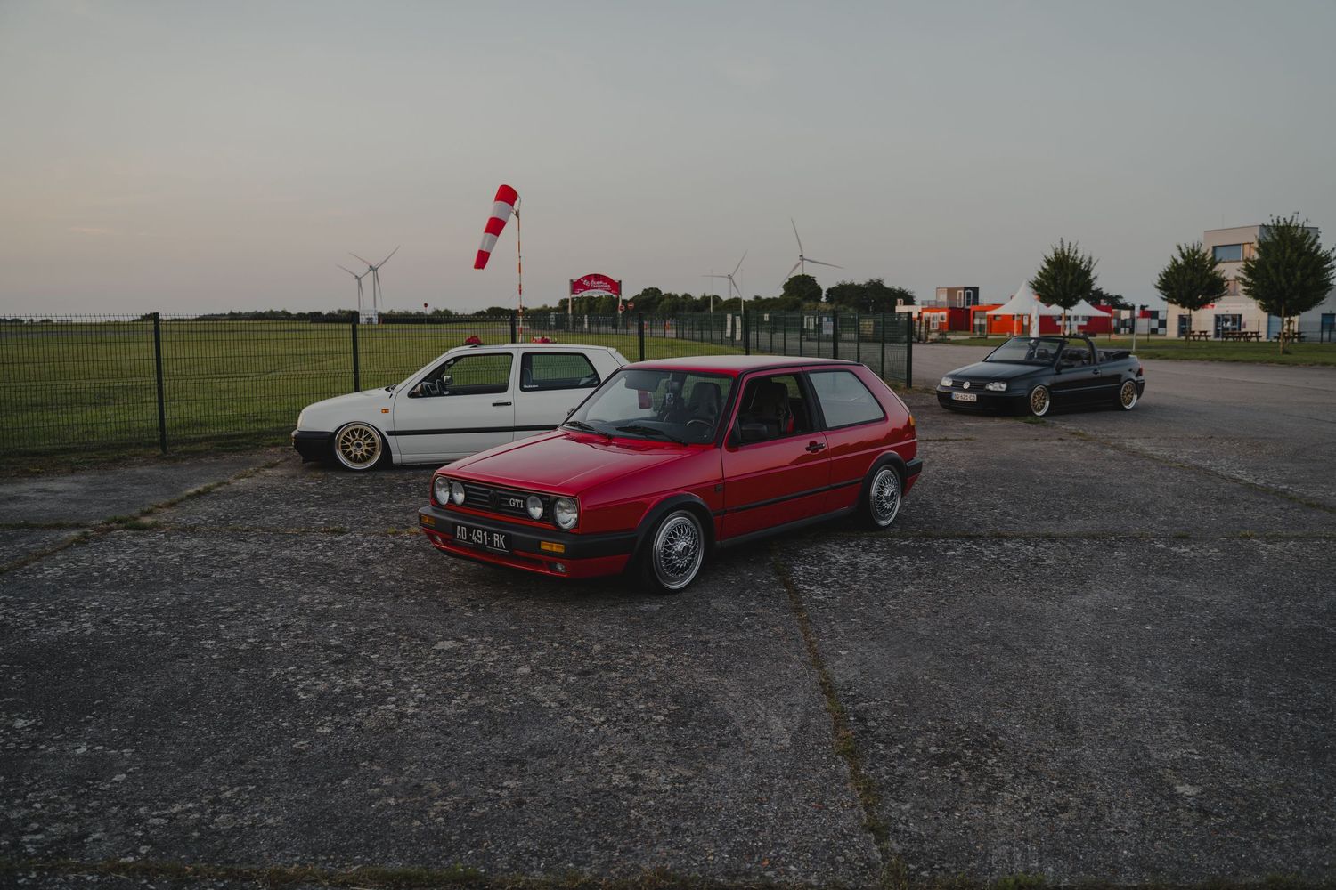 Vintage cars parked in a row on gravel lot at sunset.