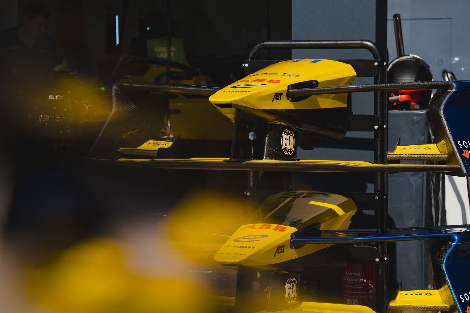 Yellow Formula E racing car components displayed in a garage pit lane during a motorsport event.
