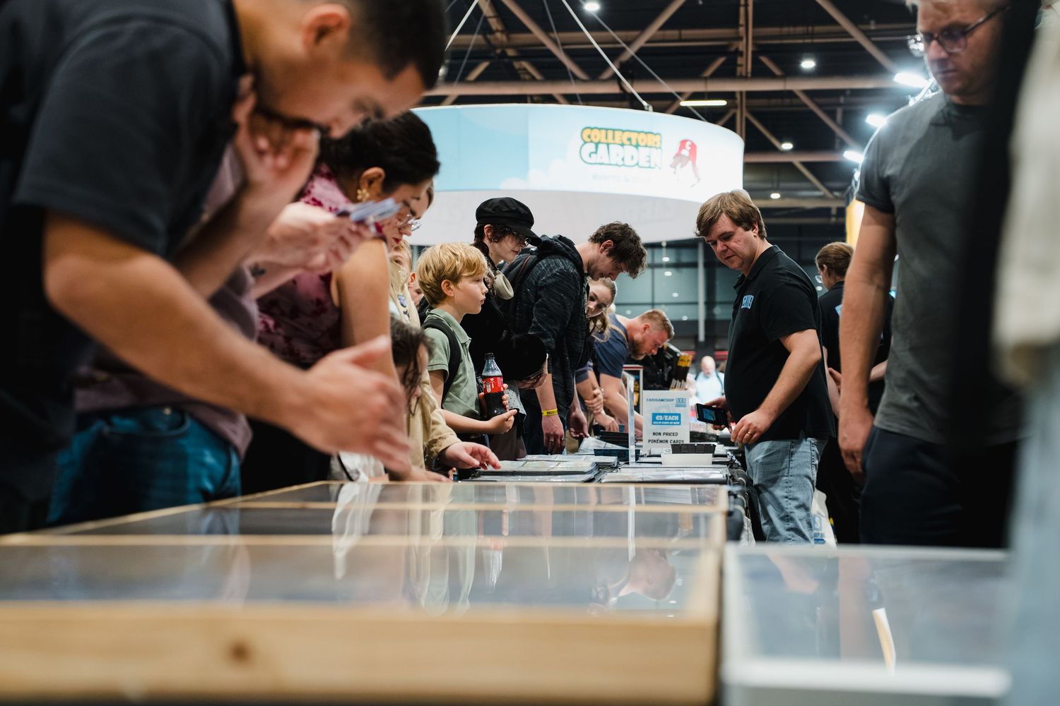 Crowd of people gathered around a long table at an indoor exhibition or trade show event.