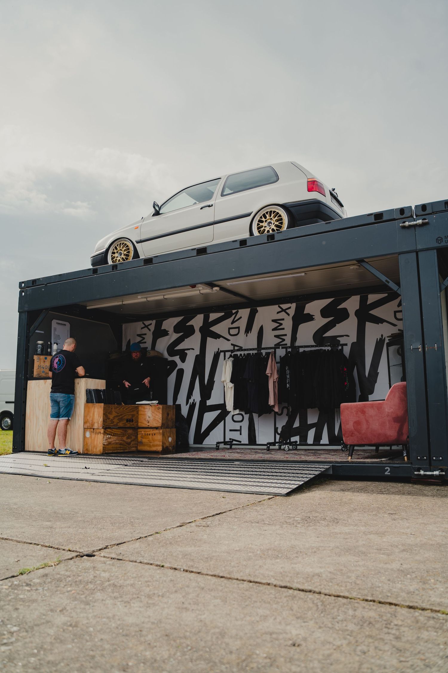 Modified white hatchback car displayed on top of a shipping container with street art.