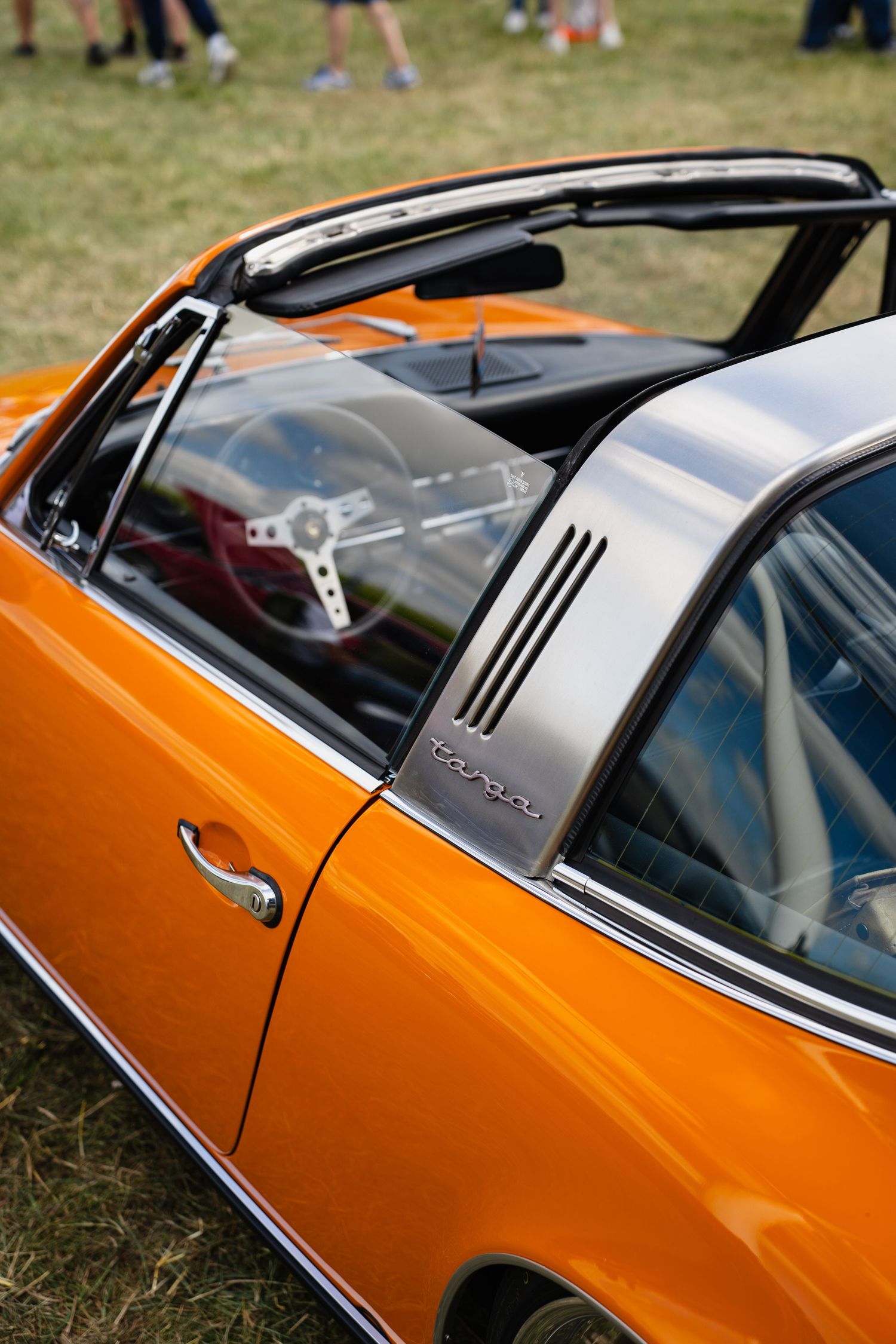 Vintage orange Porsche 911 Targa with chrome roll bar and vented C-pillar at a classic car show.
