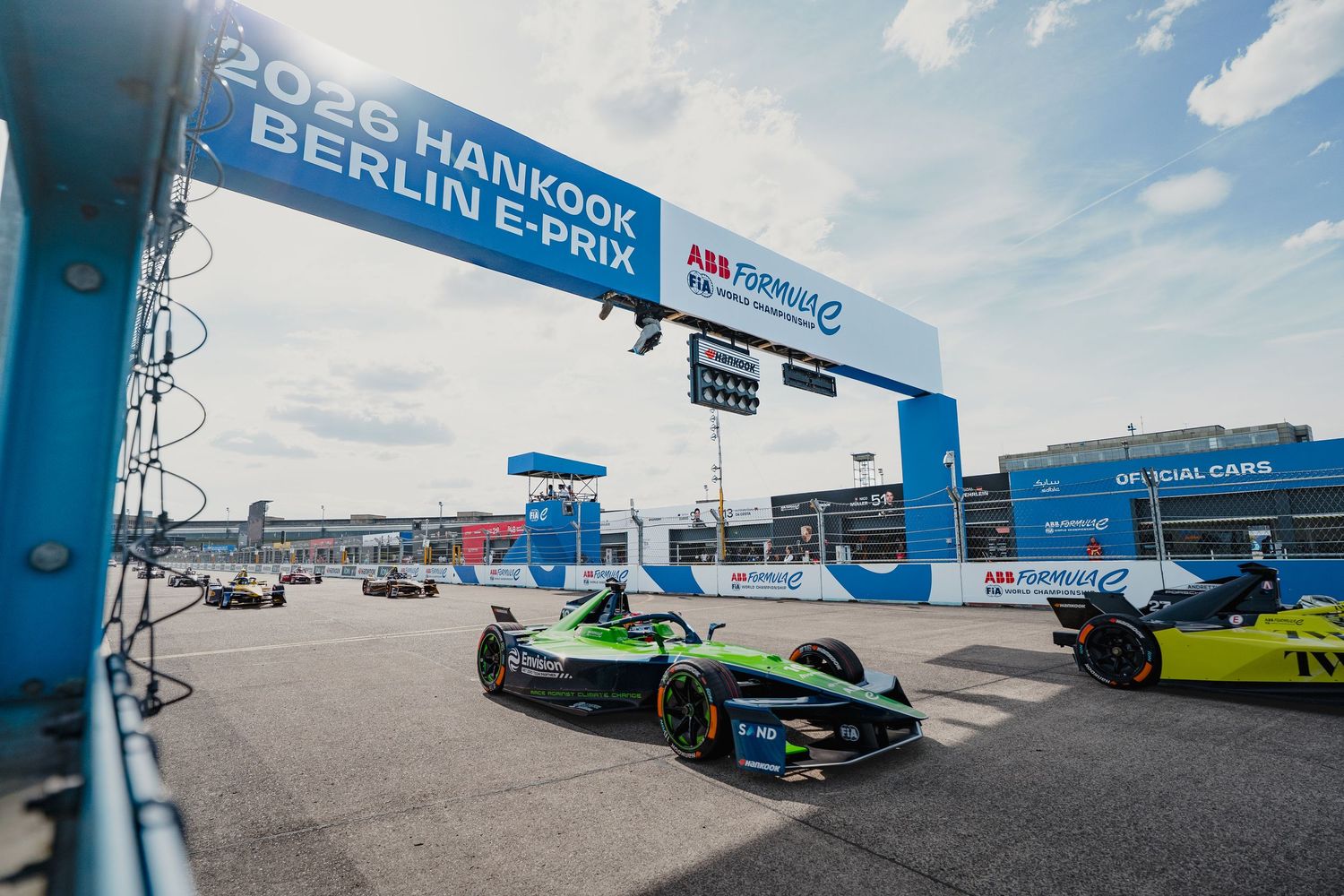 Green Formula E car races at the 2026 Hankook Berlin E-Prix on a sunny day with competitors visible in the background.