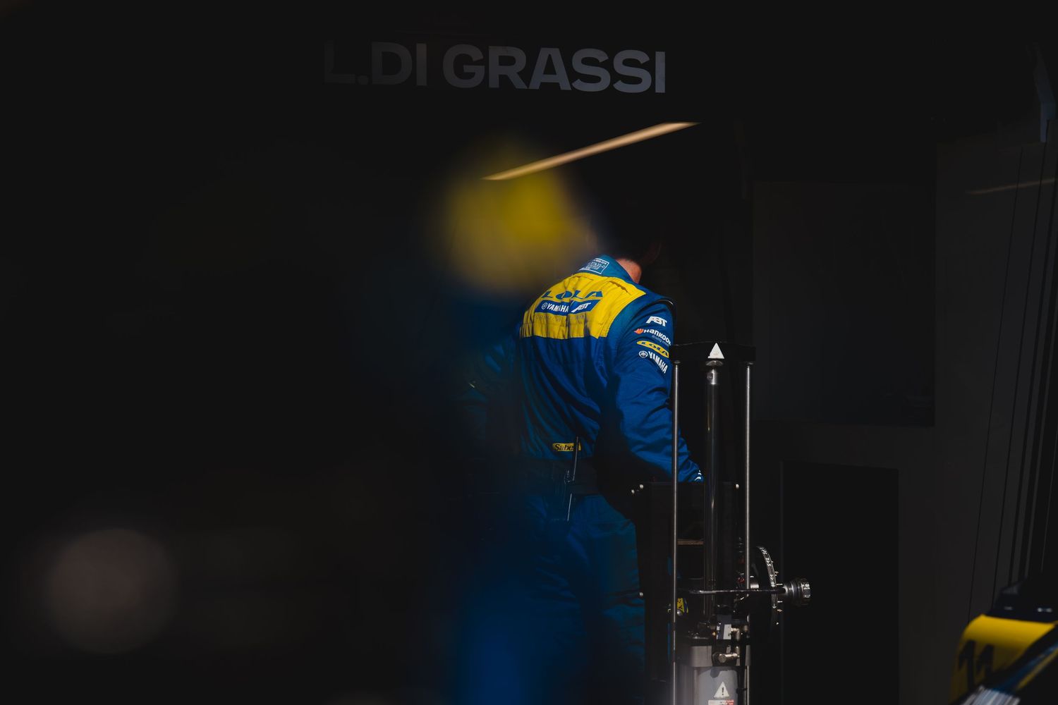 Lucas di Grassi in racing suit stands in a dimly lit pit garage during a Formula E race event.