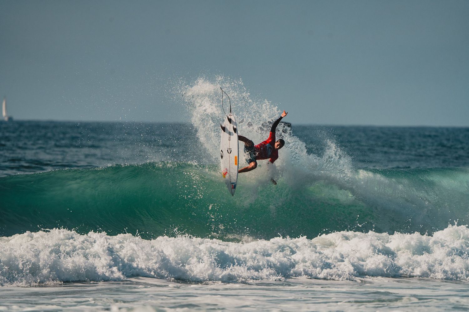 A surfer performs an aerial maneuver above a crashing wave.