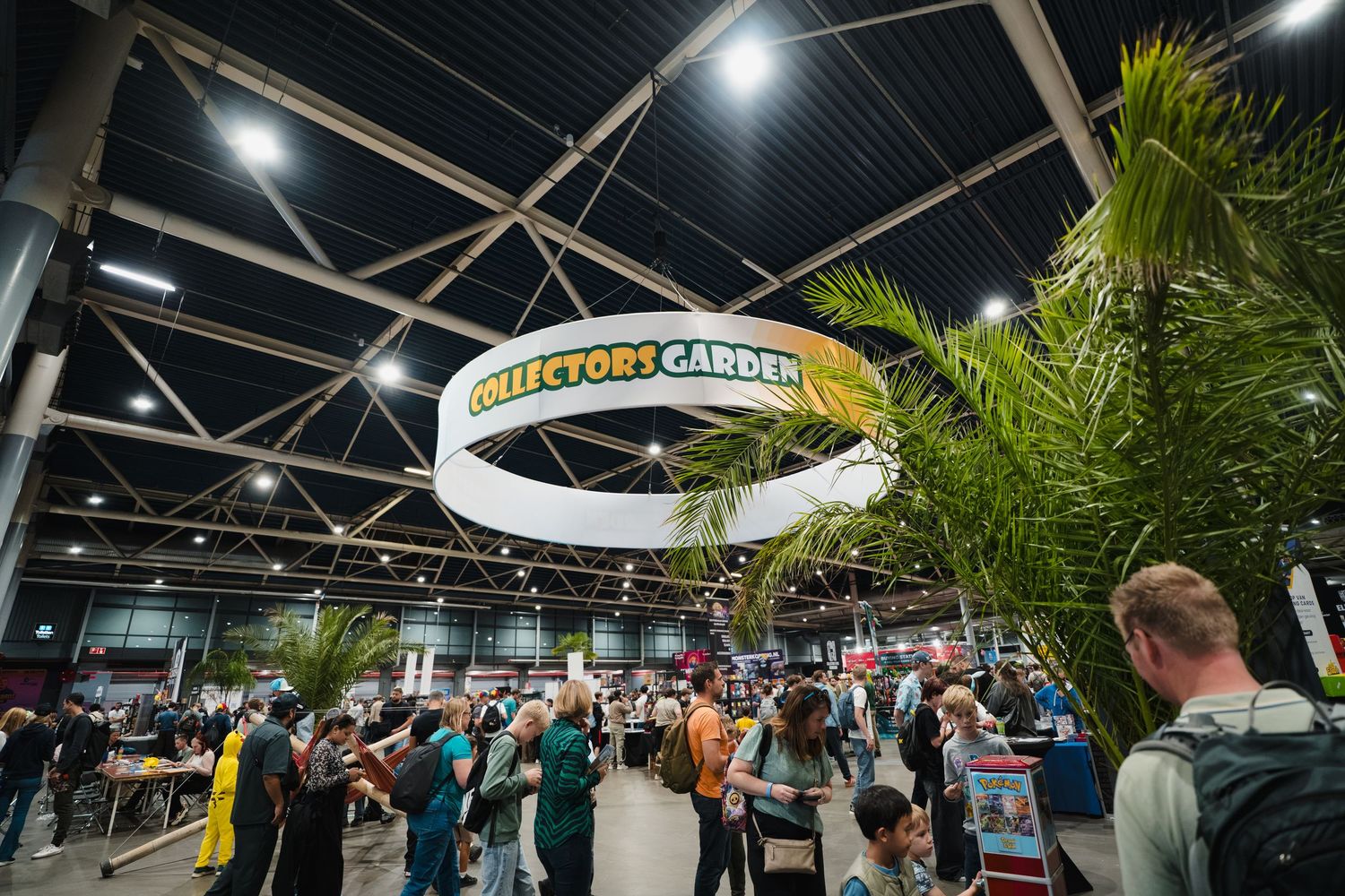 Crowded Collectors Garden exhibit hall with tropical plants and circular sign at an indoor convention event.
