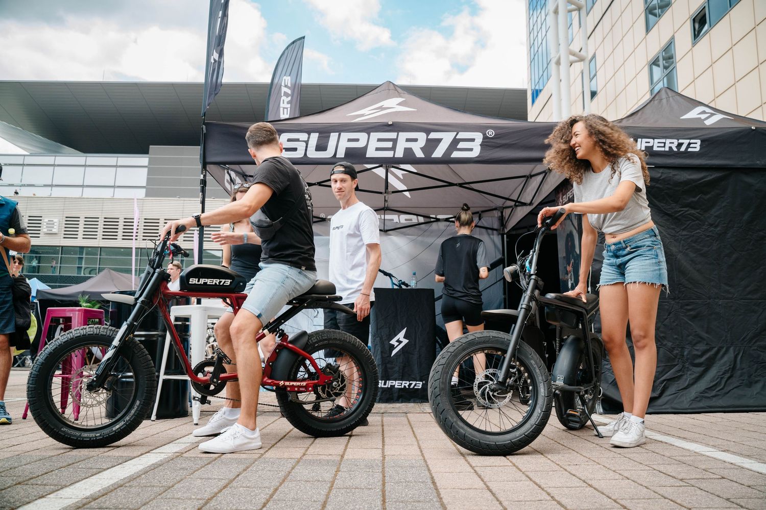 Super73 electric bike display outdoors with people examining the bikes under a branded tent.