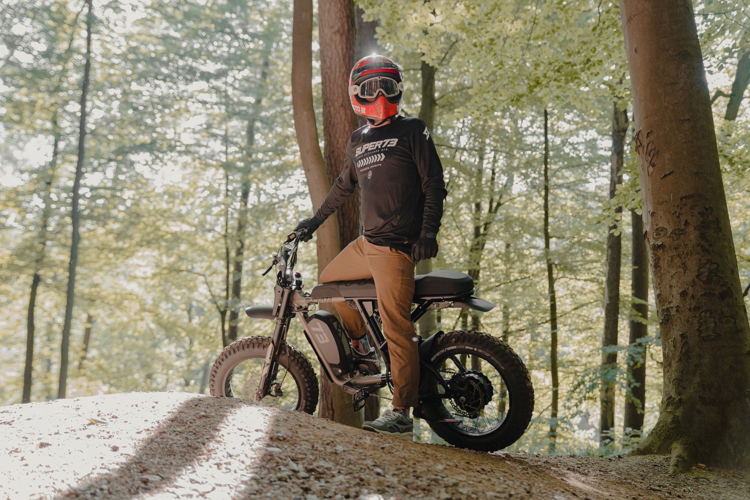 A rider stands with their off-road motorcycle on a forest dirt path.