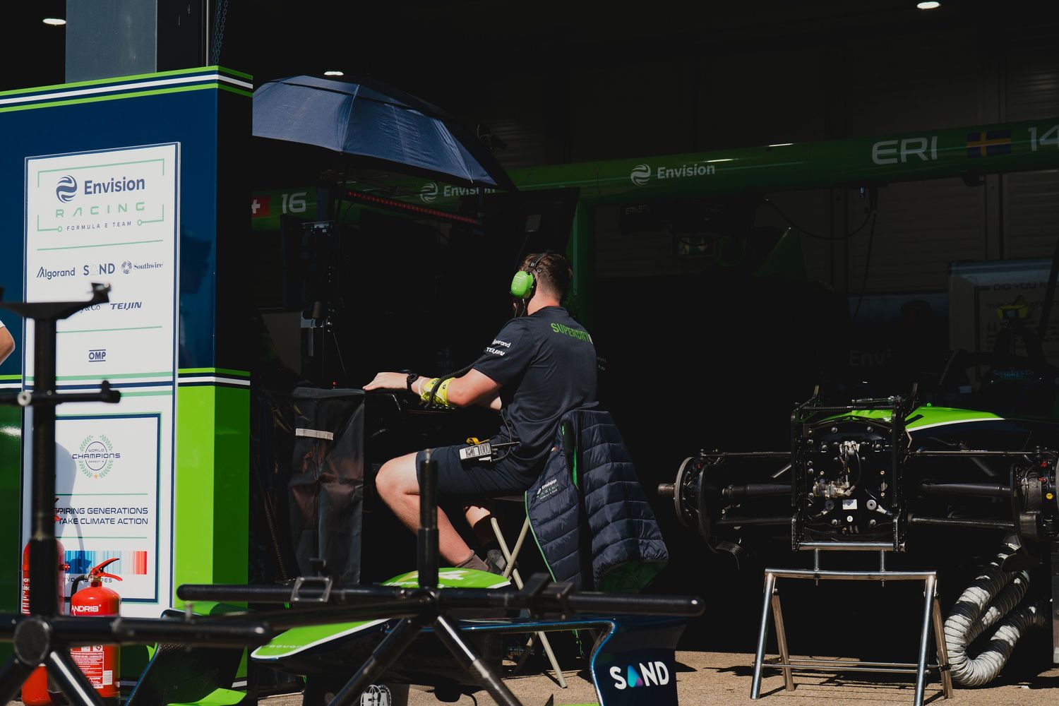A technician in green headphones works at an Envision Racing pit garage during a Formula E race event.