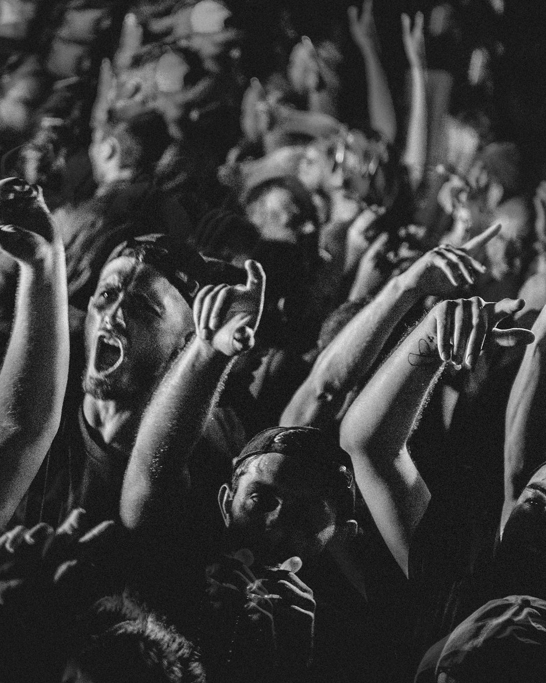 Black and white photo of a crowd at a concert with raised hands creating an energetic atmosphere.