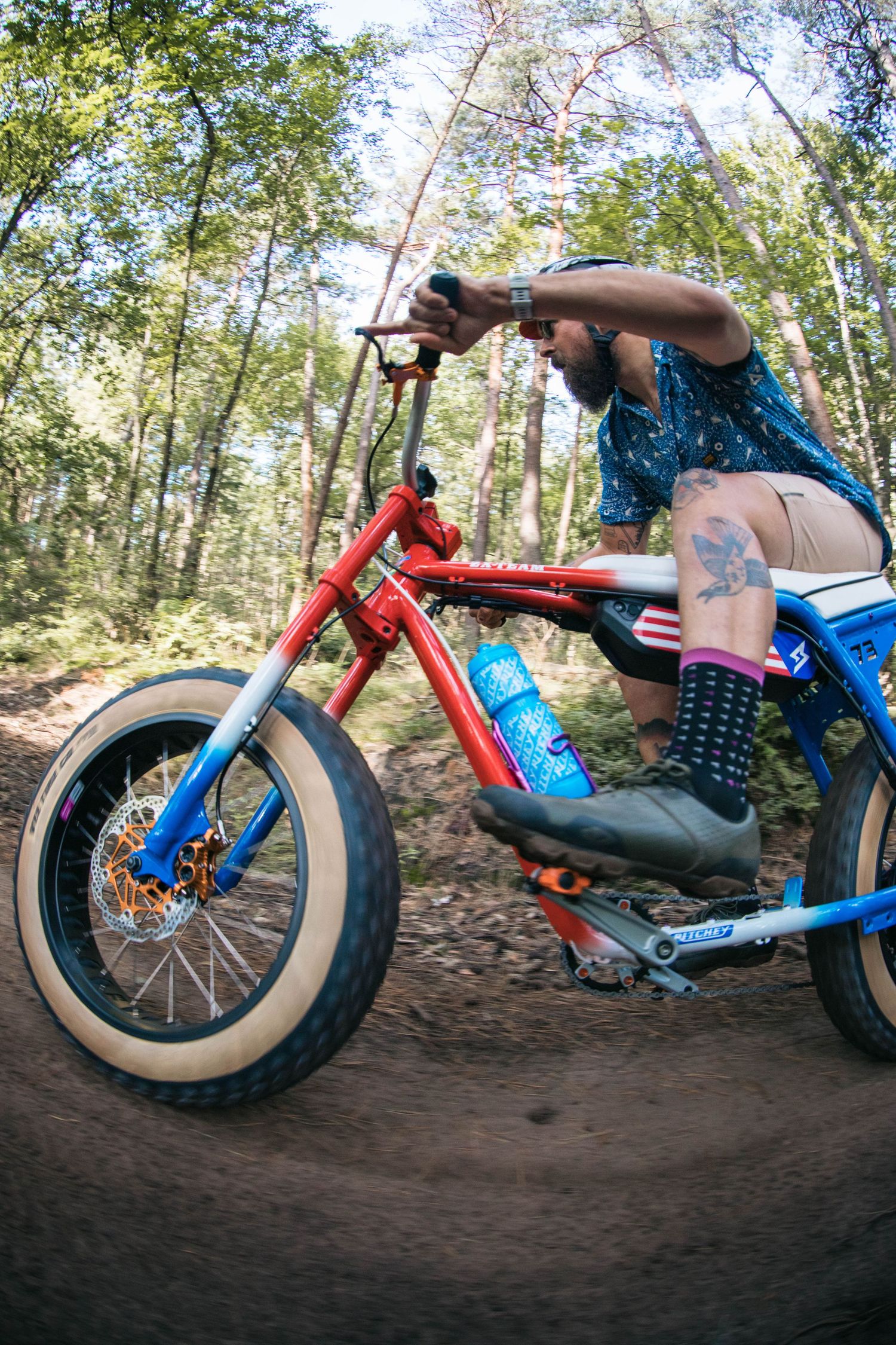 Sequence of a red and blue custom bike performing a dirt jump trick on a forest trail.