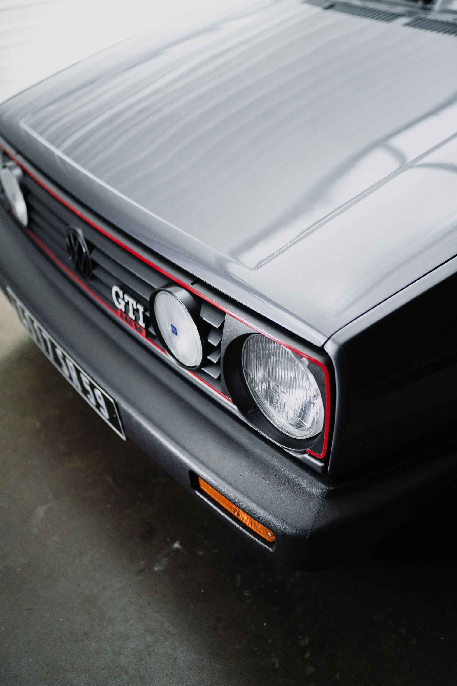 Close-up of a classic Volkswagen Golf GTI front grille and headlight in silver with red accent stripe.