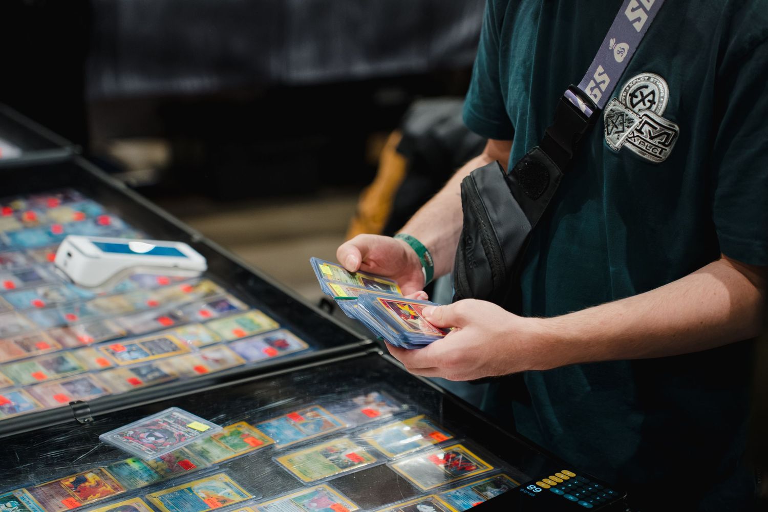 Person browsing and handling collectible trading cards displayed in a binder at a card show or hobby shop.