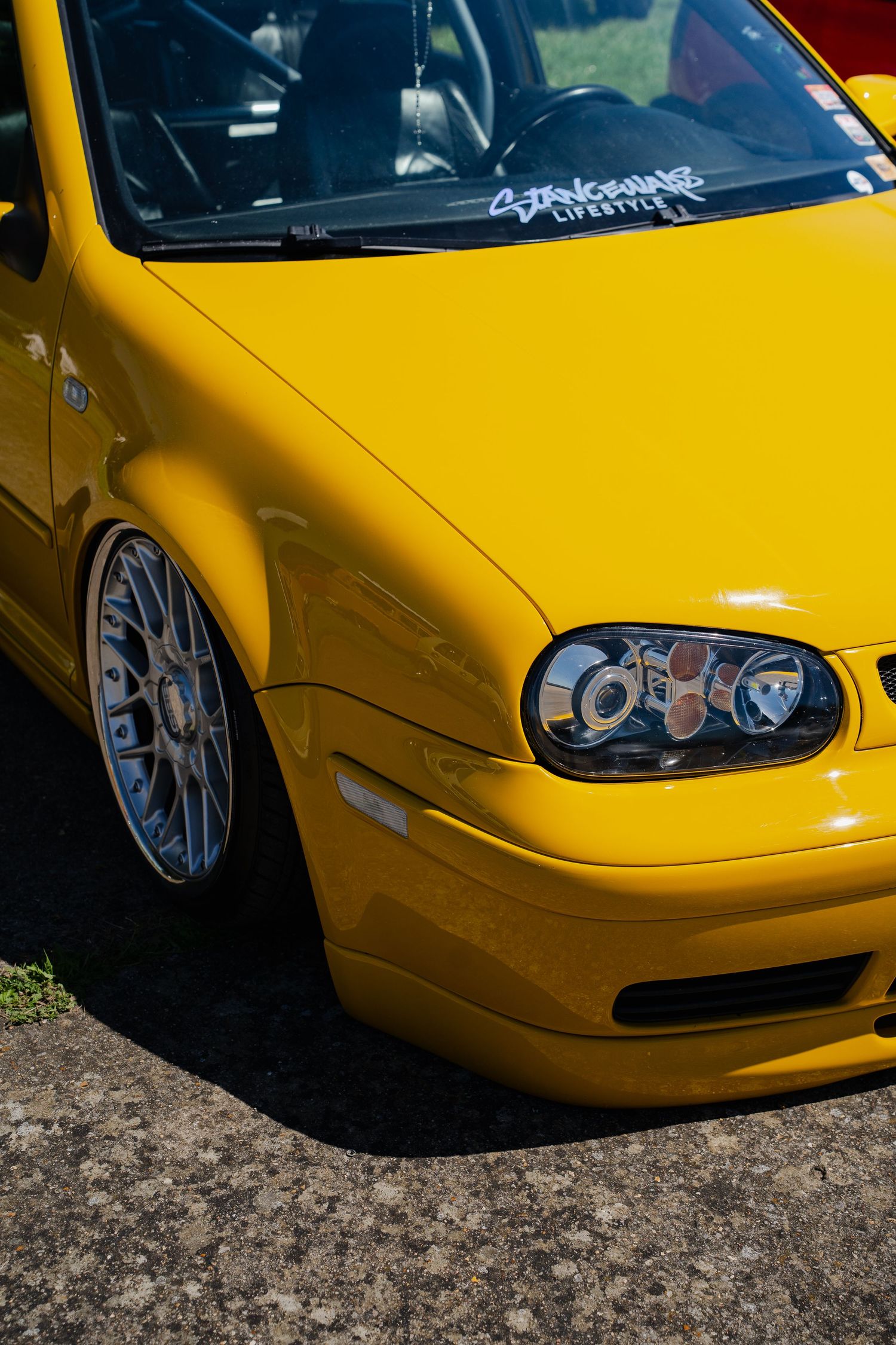 Bright yellow modified Volkswagen Golf Mk4 with polished BBS wheels, lowered stance, and custom headlights at a car show.