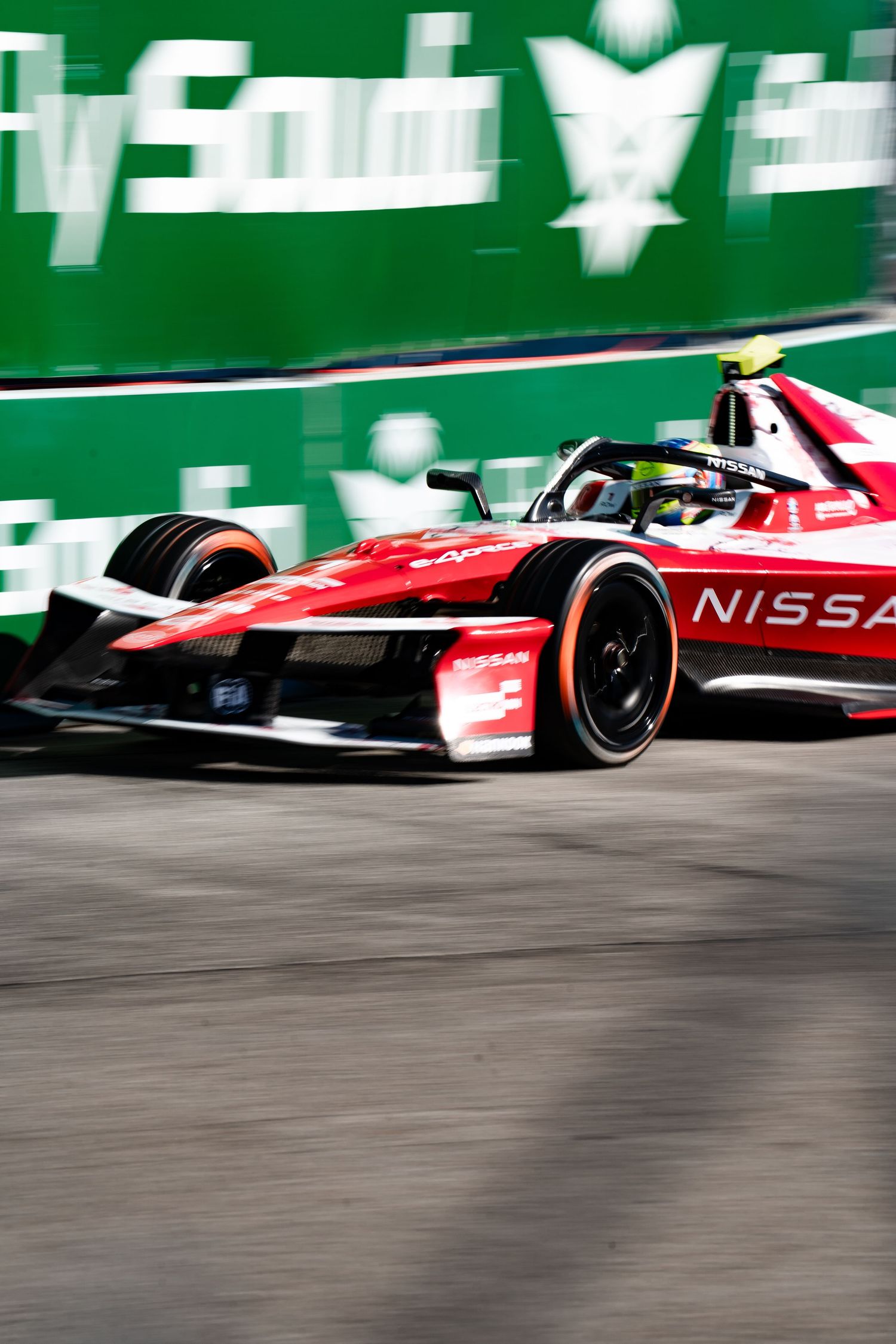 Nissan Formula E race car speeding on track with Fly Saudia green barrier in background during competitive circuit event.
