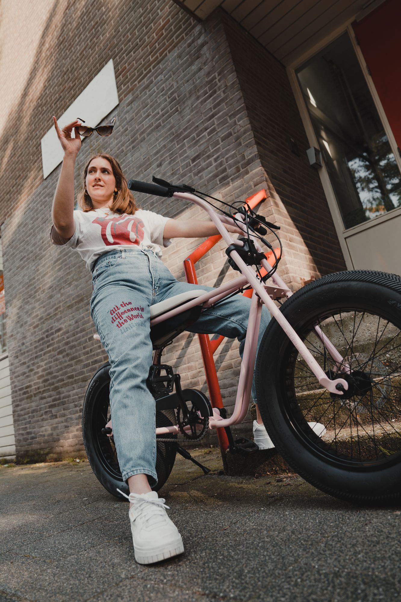 Person on white fat tire bike posing against brick wall with casual style.