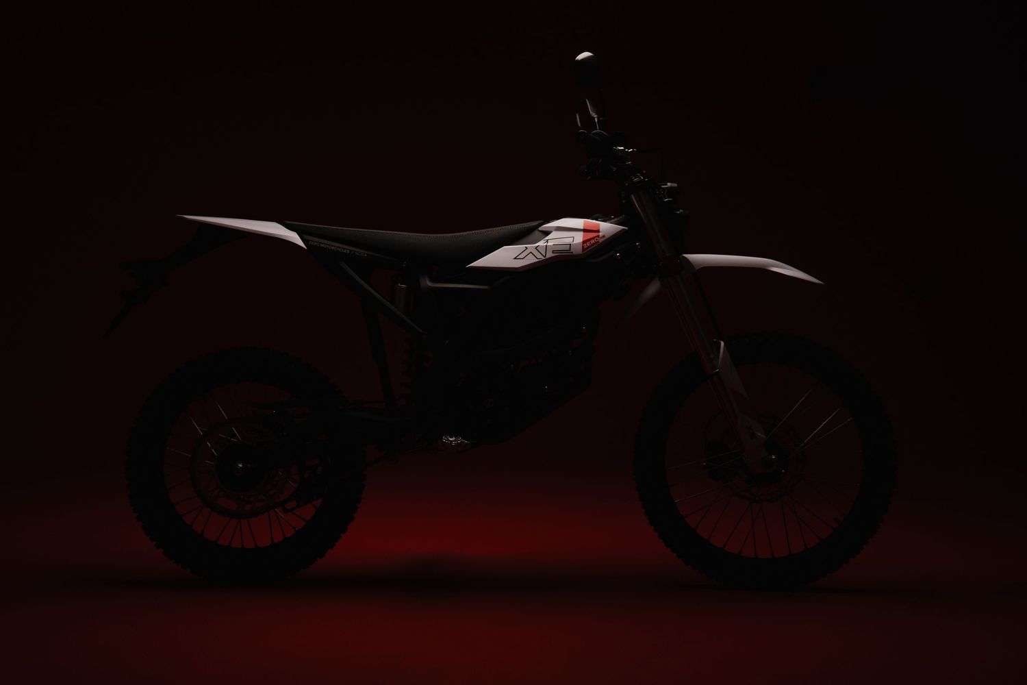 Silhouette of electric dirt bike photographed against dark red background.