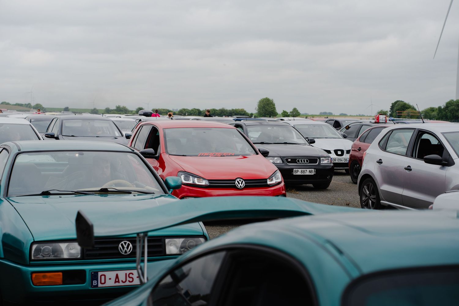 A crowded parking lot filled with various Volkswagen and other cars under an overcast sky.