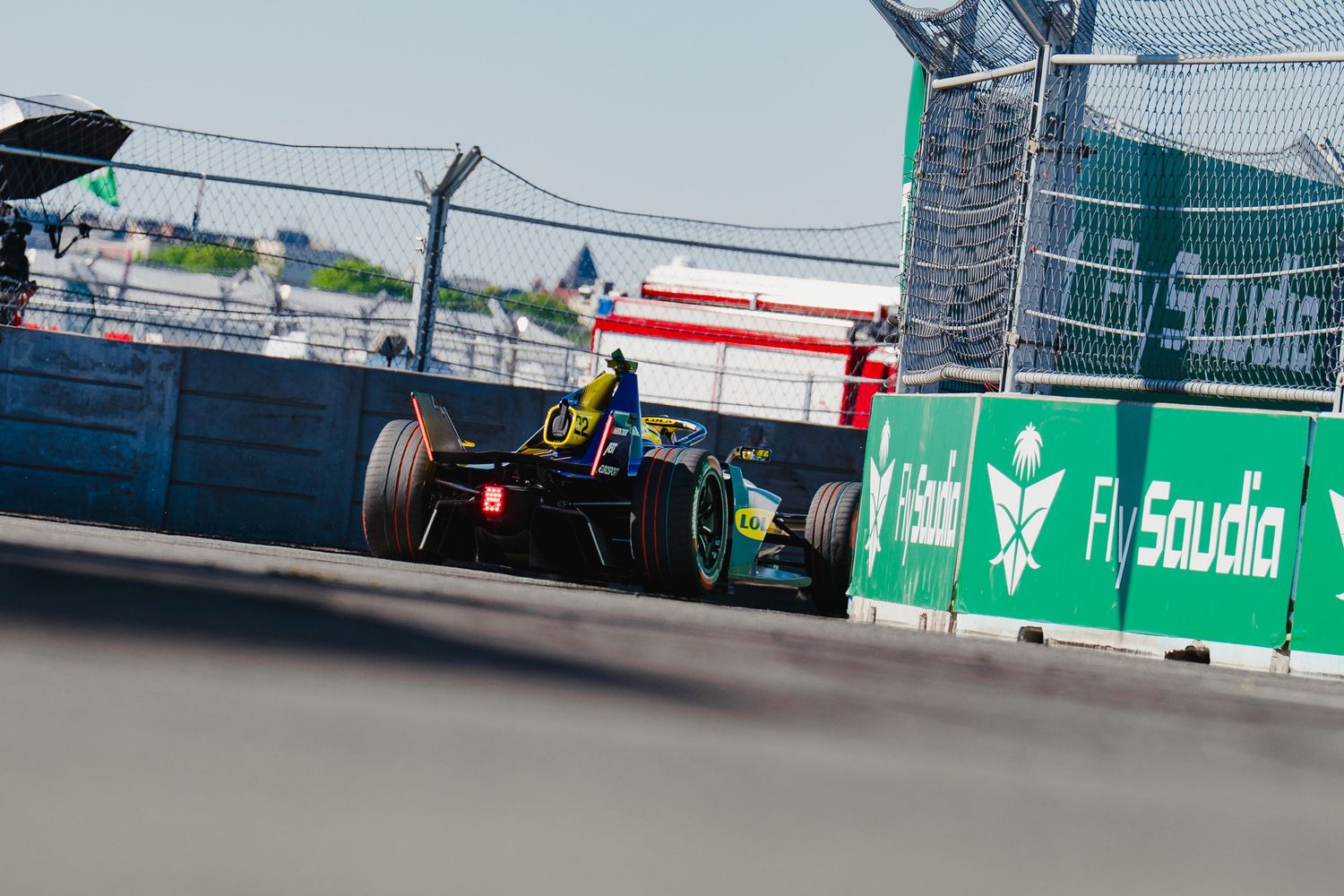 A Formula racing car speeds past Fly Saudia advertising boards on a street circuit during a race event.