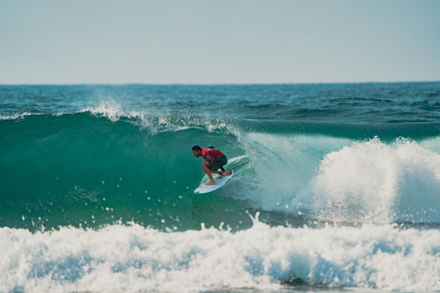 A surfer rides the face of a turquoise wave during a surfing session.