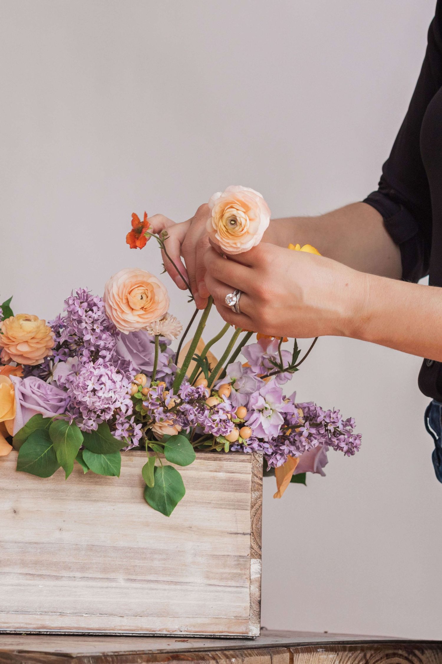 florist in black shirt placing light orange ranunculus in planter box arrangement