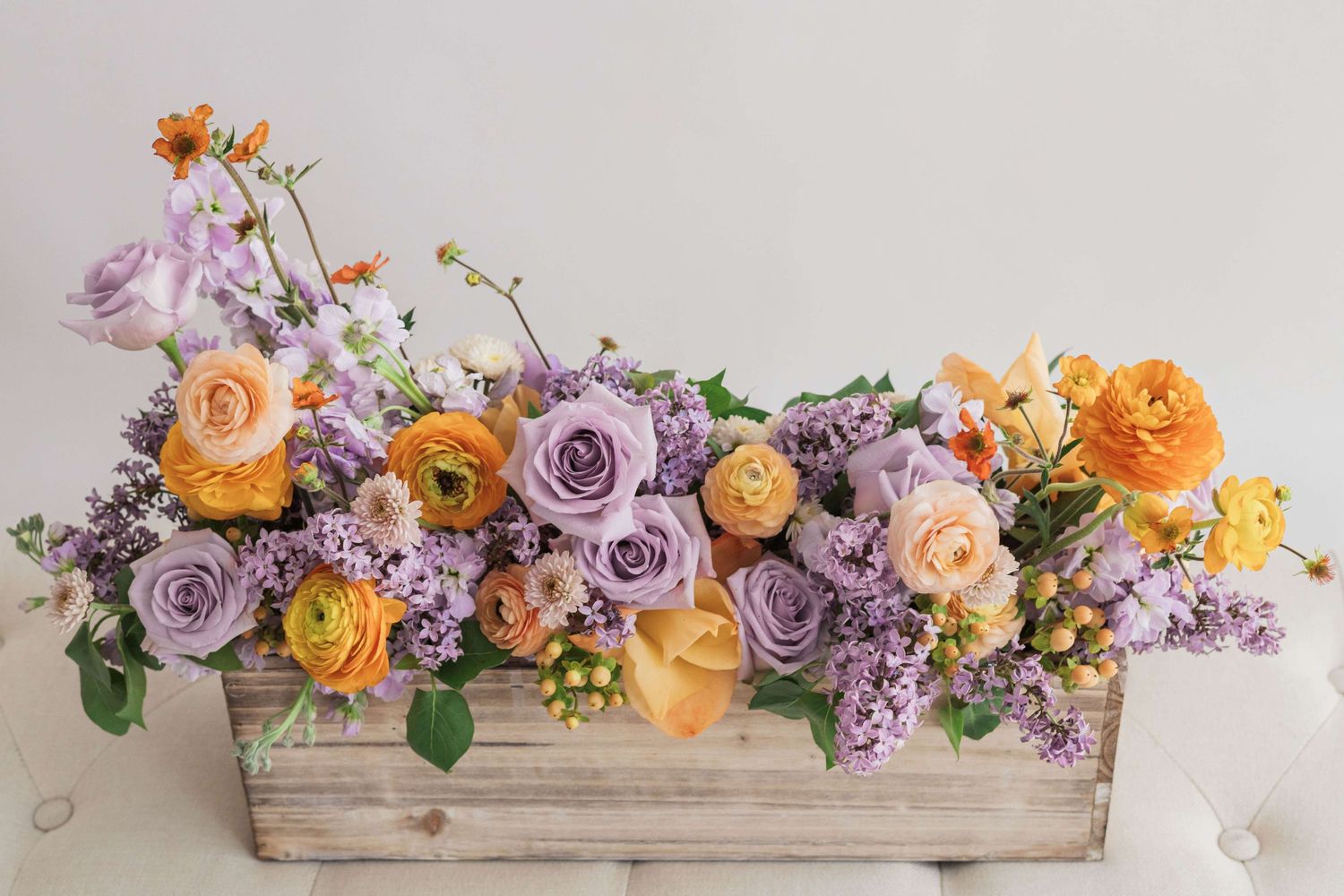 Planter box arrangement with orange and purple ranunculus lilac roses geum stock flower hypercium