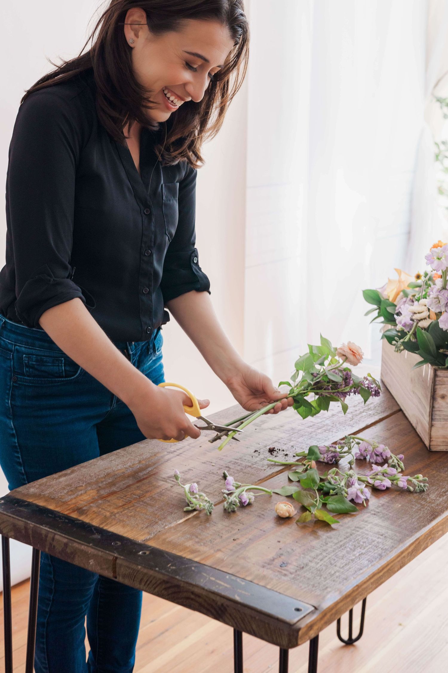 florist smiling while trimming stems of flowers about to go into planter box arrangement