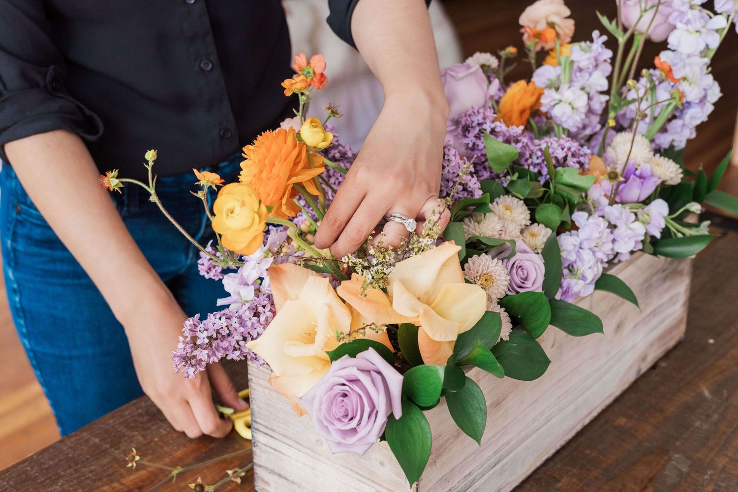 adjusting orange ranunculus in planter box with orange and purple lilacs roses geum stock flower and hypercium