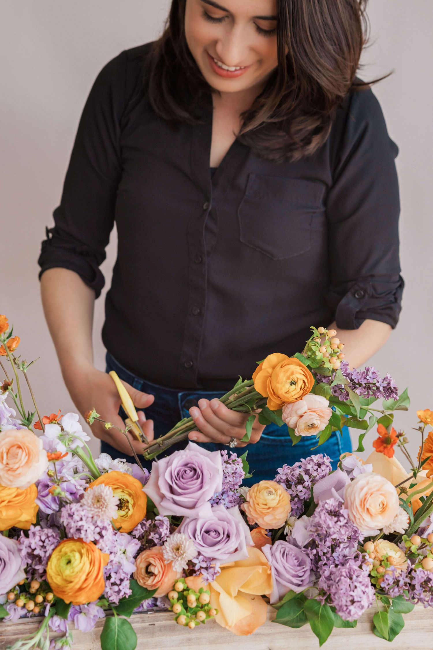 Florist holding ranunculus and roses behind planter box arrangement