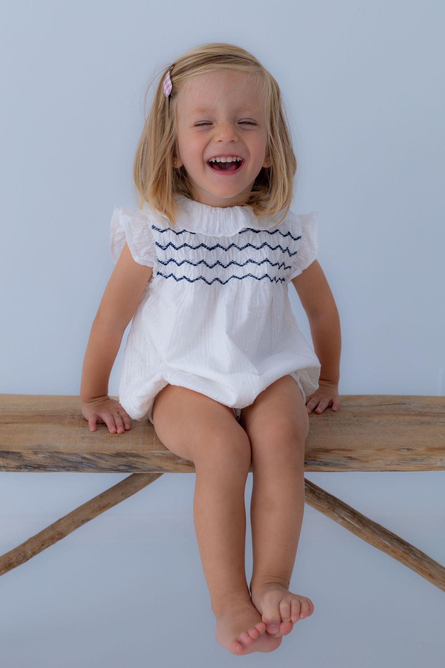 Foto de risa espontánea de niña sobre banco de madera en estudio de luz natural. Sesión infantil y familiar en Valdemoro, zona sur Madrid.