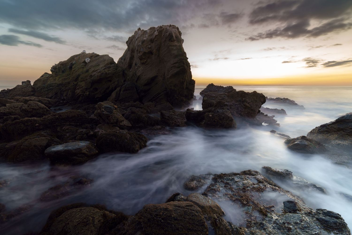 Cinematic landscape photograph of a dramatic sunset over the rocky cliffs and crashing waves of Laguna Beach California by Vince Shewmaker.