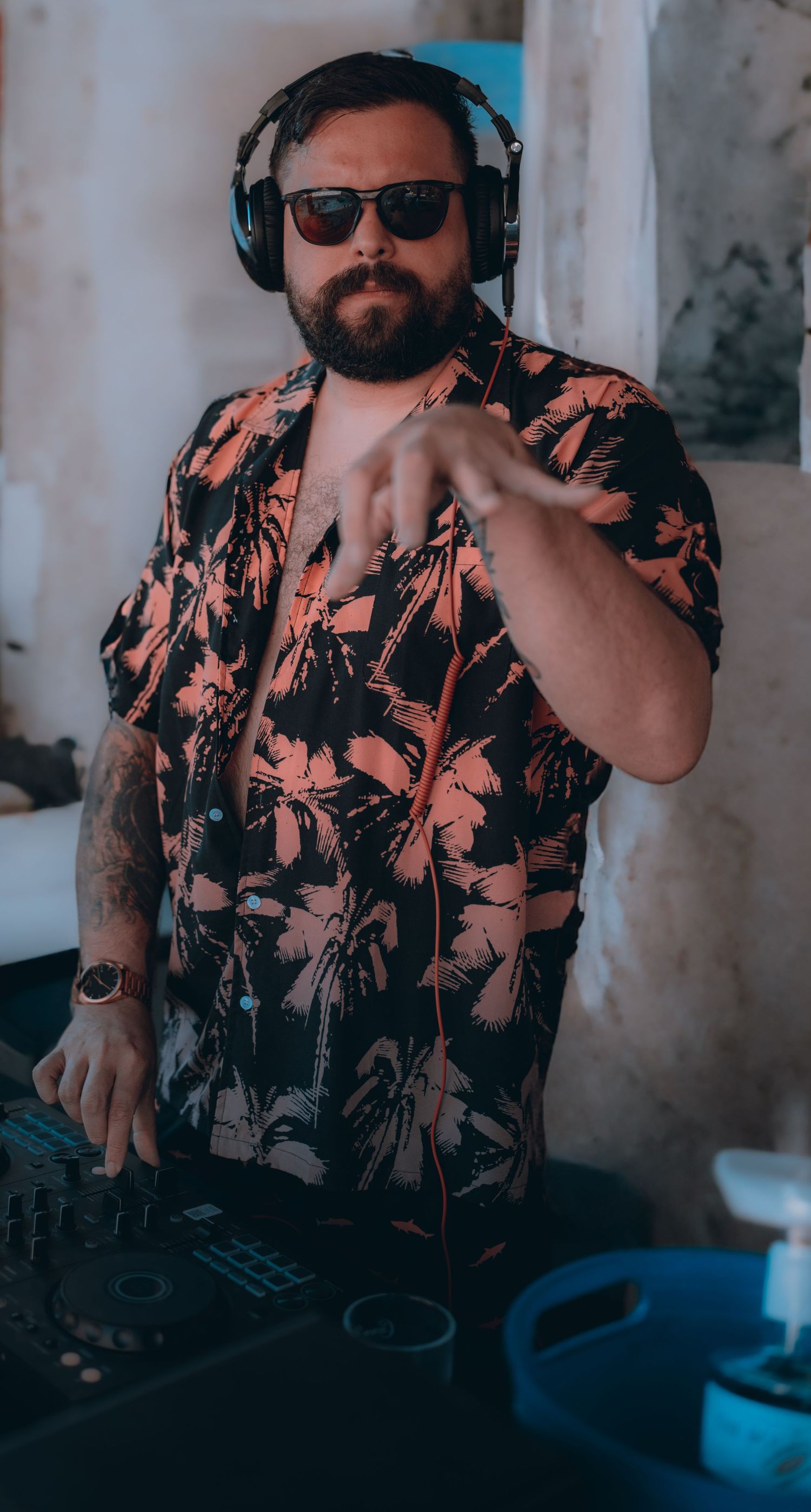 DJ in floral shirt and headphones performing at mixing deck.