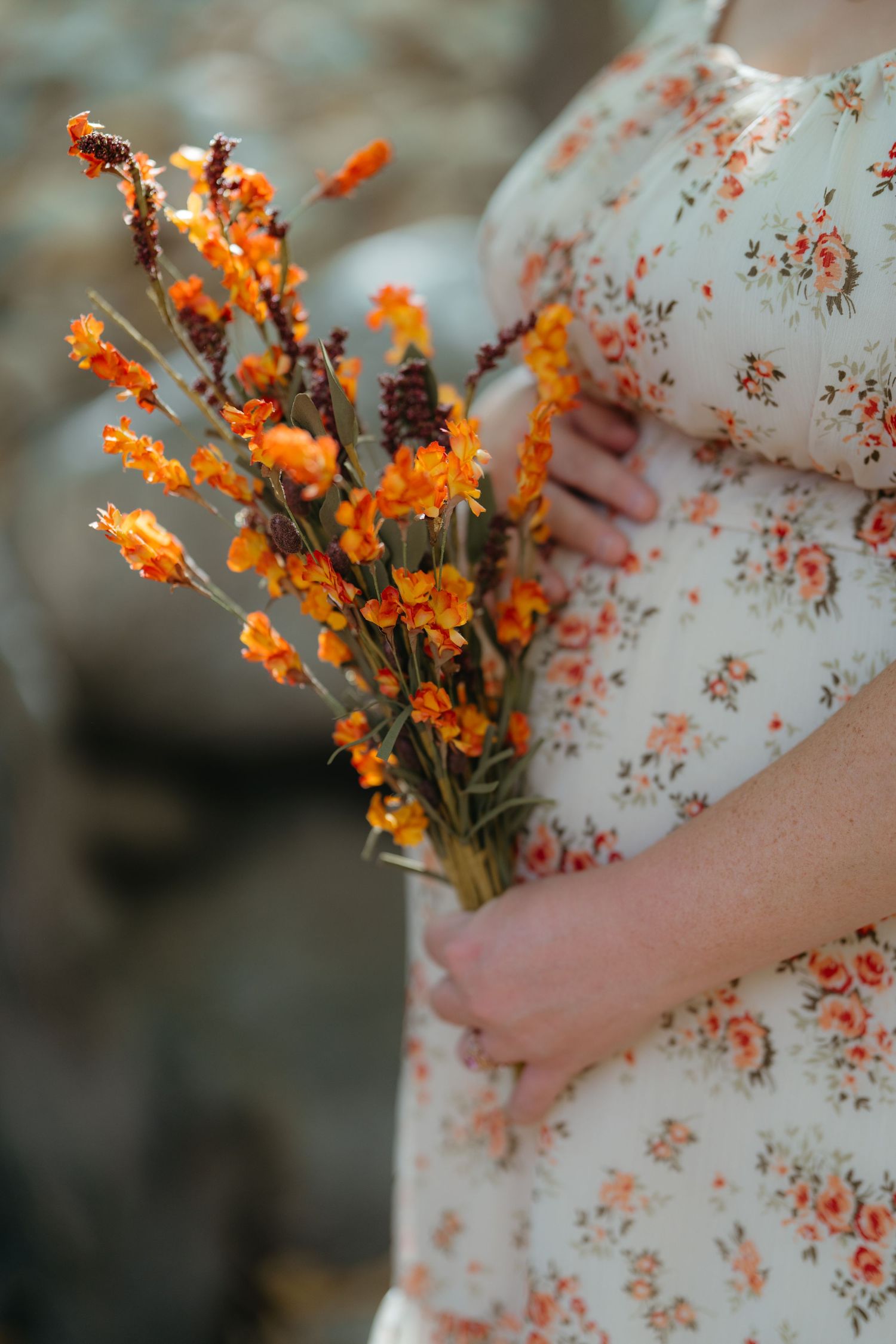 Orange wildflowers held against a floral dress in soft natural lighting.