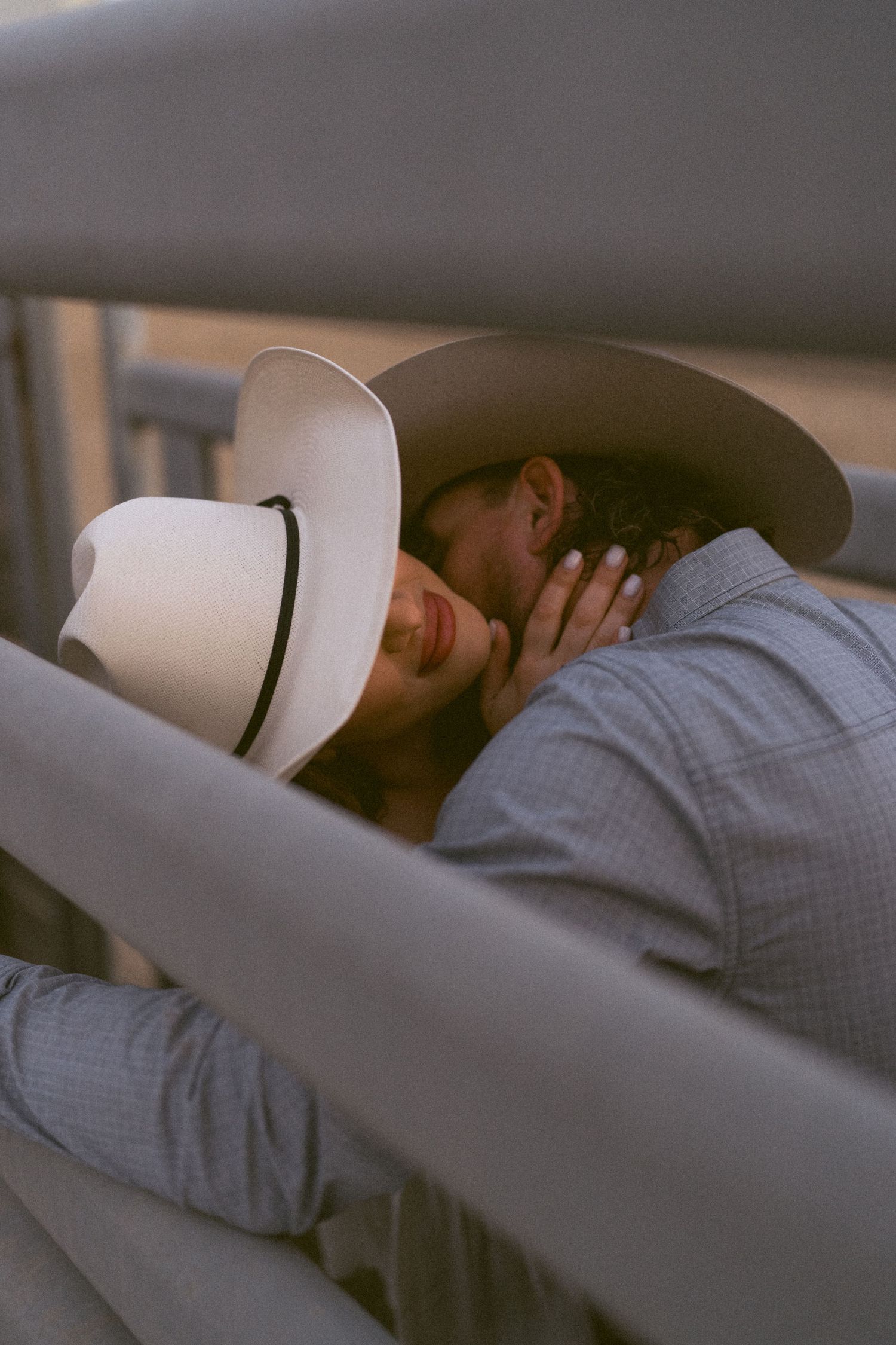Intimate moment between couple wearing cowboy hats in soft lighting.