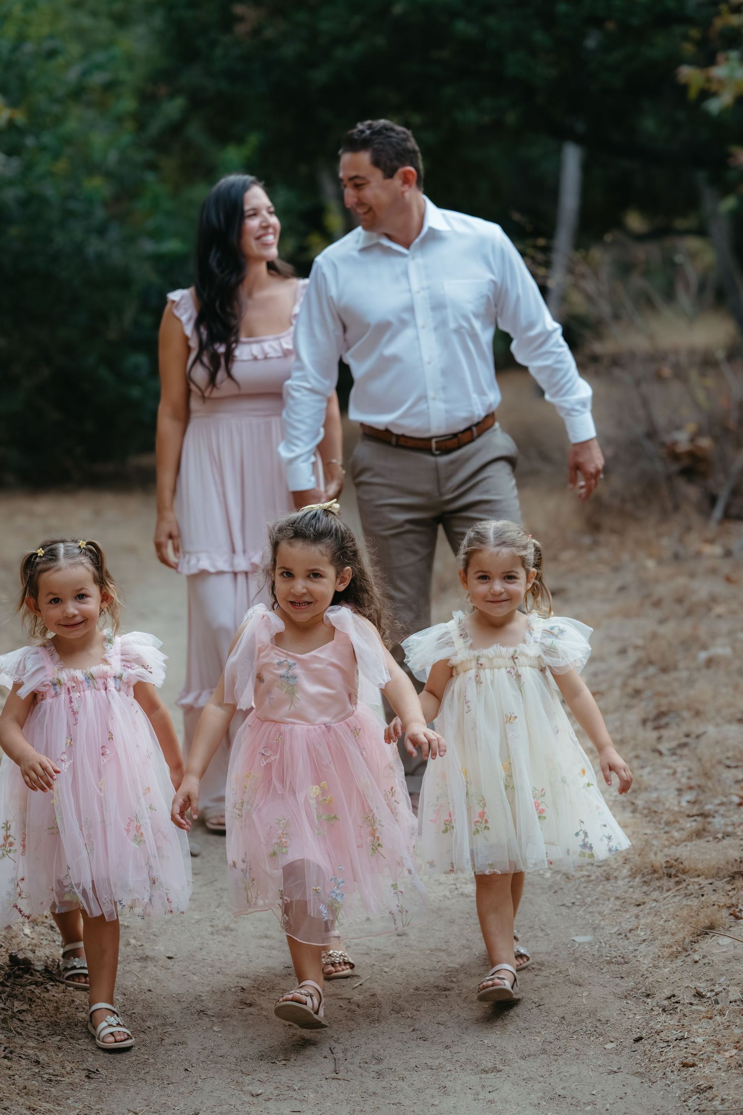 Family walking together on path wearing coordinated pink and white outfits.