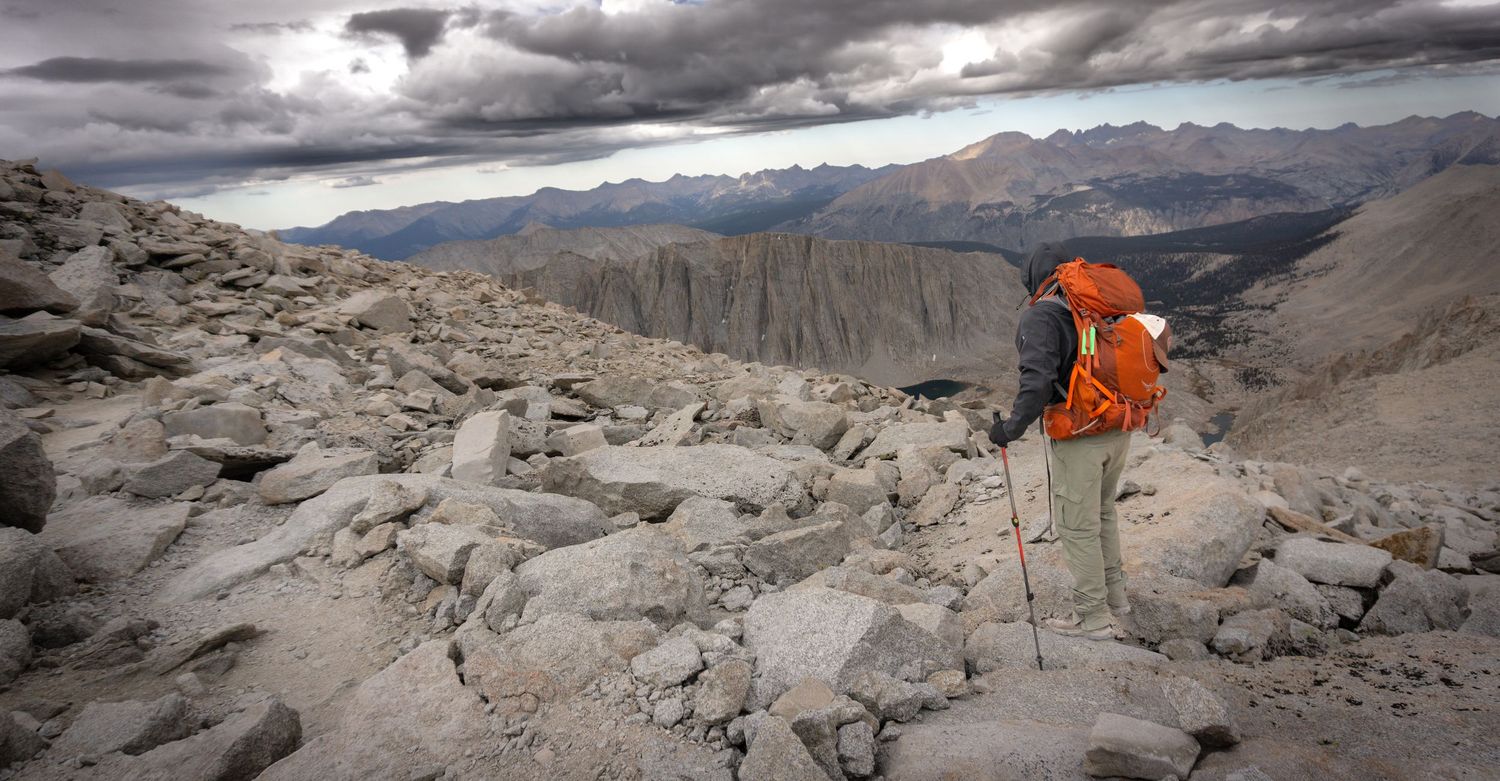 Dramatic mountain landscape with snow-capped peaks and rocky terrain under cloudy skies.