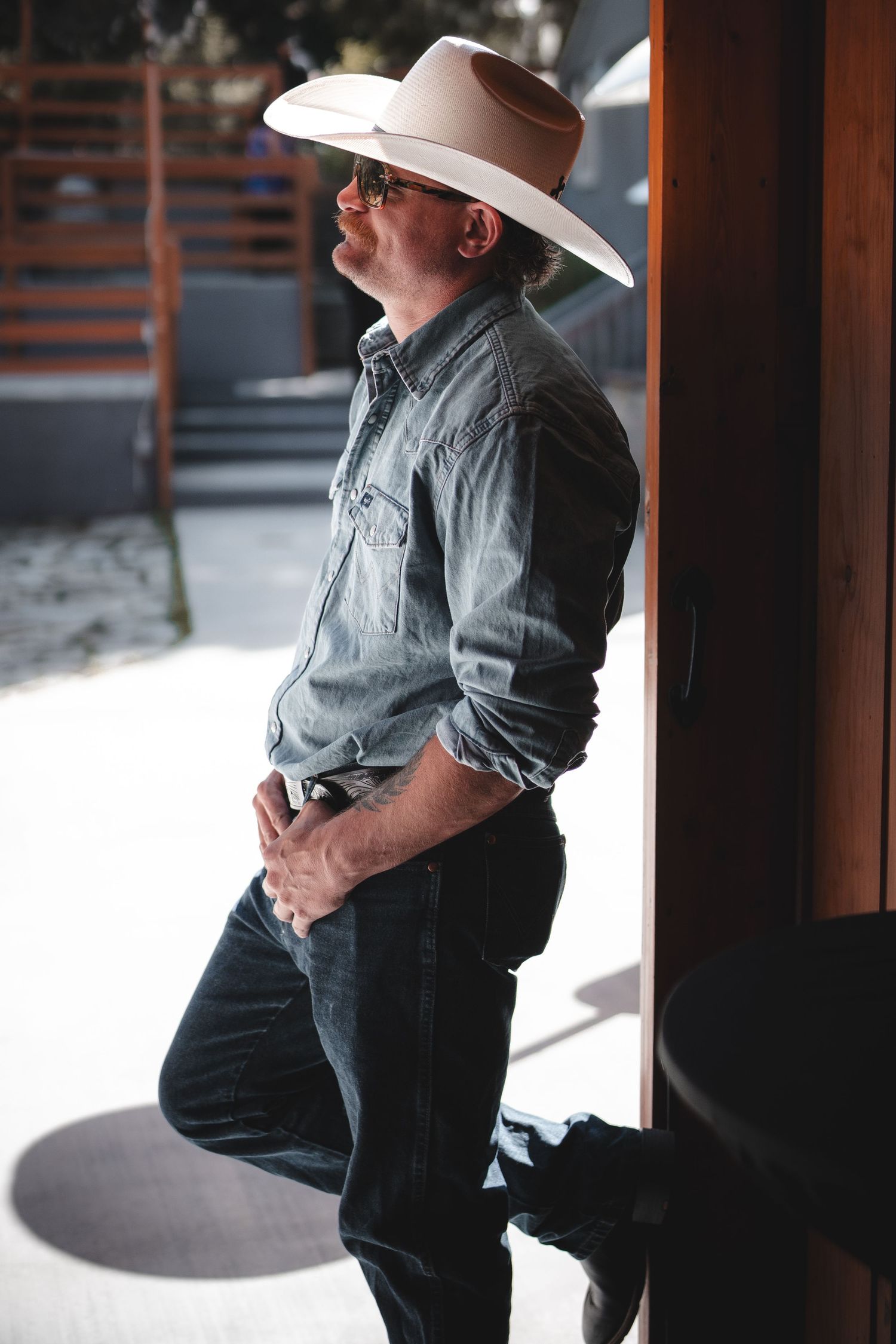 Figure in western wear stands thoughtfully in doorway of rustic wooden barn.
