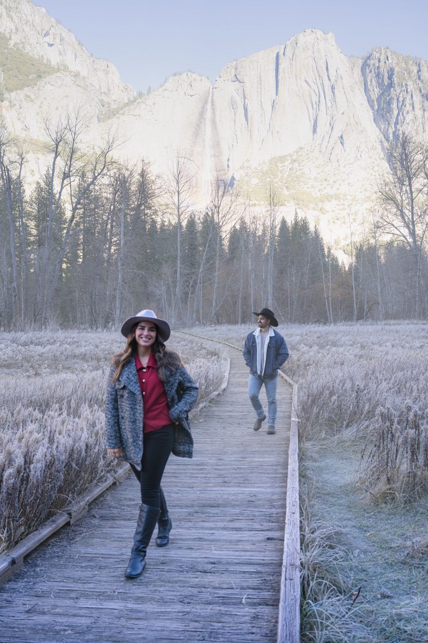People walking on a wooden boardwalk with snow-capped mountains in the background in Yosemite, California